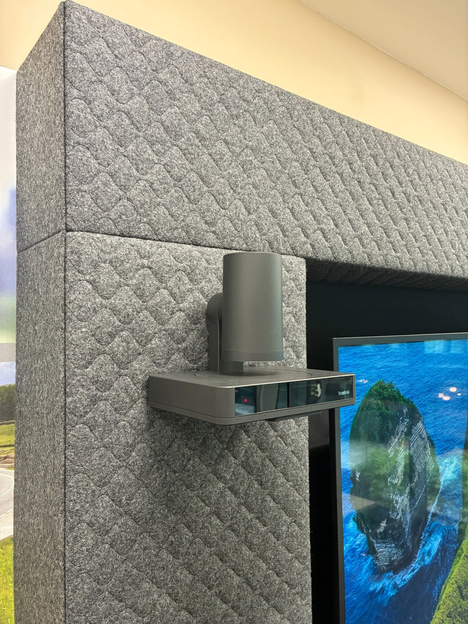 Close-up of a textured gray stone wall with a black monitor displaying a blue ocean scene with a rock and green landscape, and a gray cylindrical ventilation pipe attached to the wall.