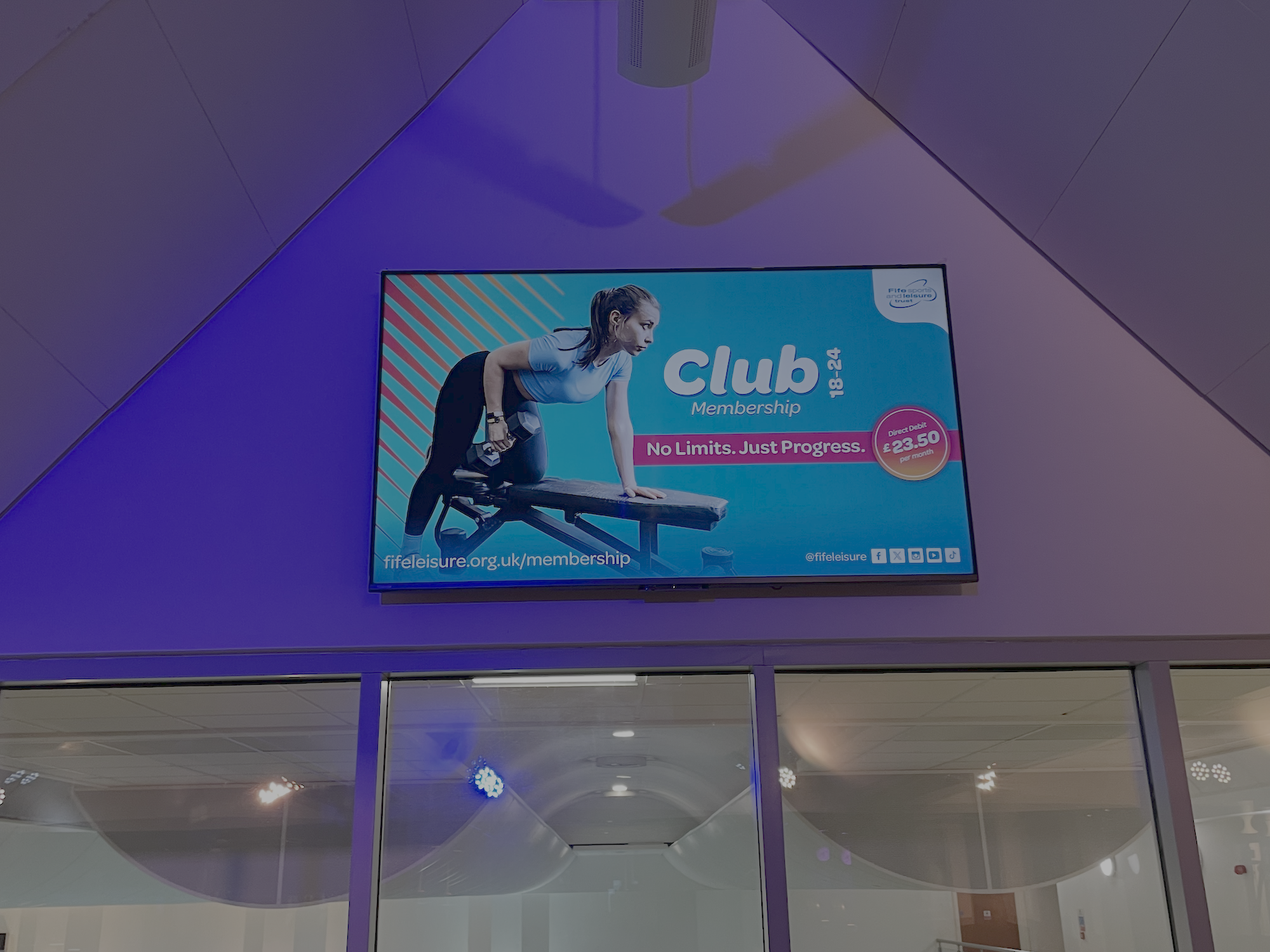 A large digital advertisement for a fitness club membership featuring a woman exercising.