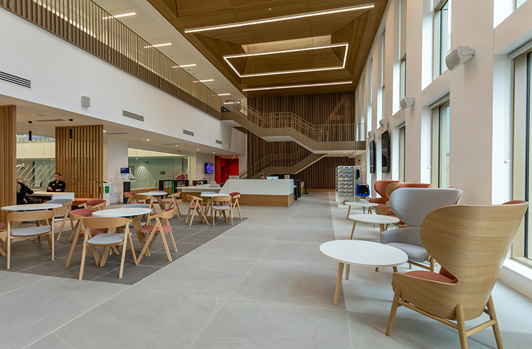 Modern indoor lounge area with wooden accents, large windows, and seating including chairs and small tables.