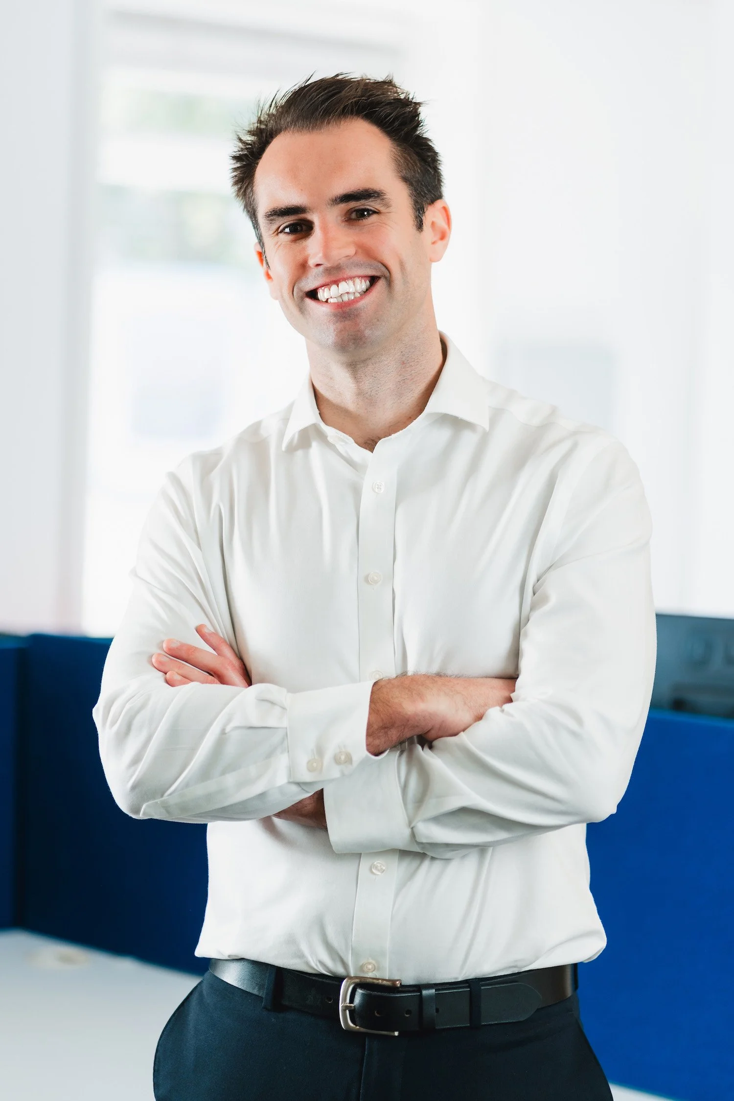 A photo of Simon smiling with his arms crossed