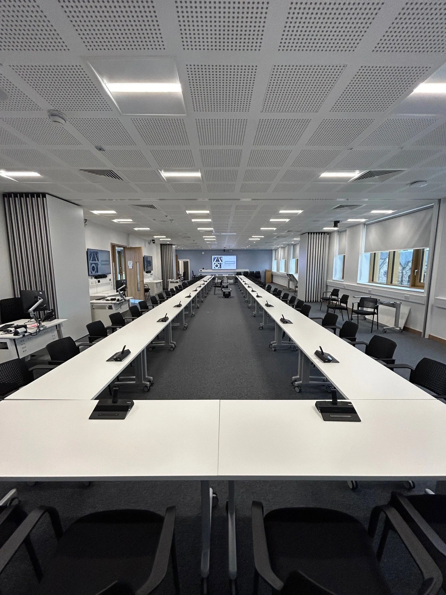 Conference room with a long tables arranged in U-shape, black chairs, and multiple monitors