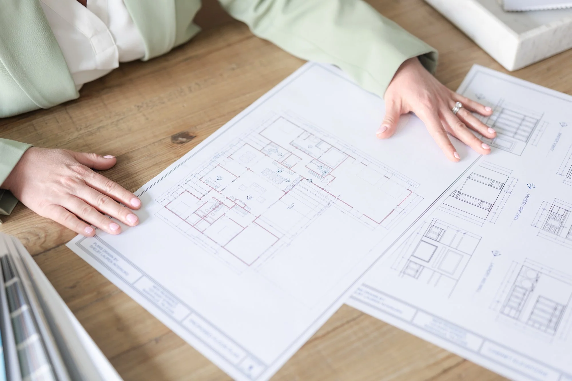 Person examining architectural blueprints on a wooden table.