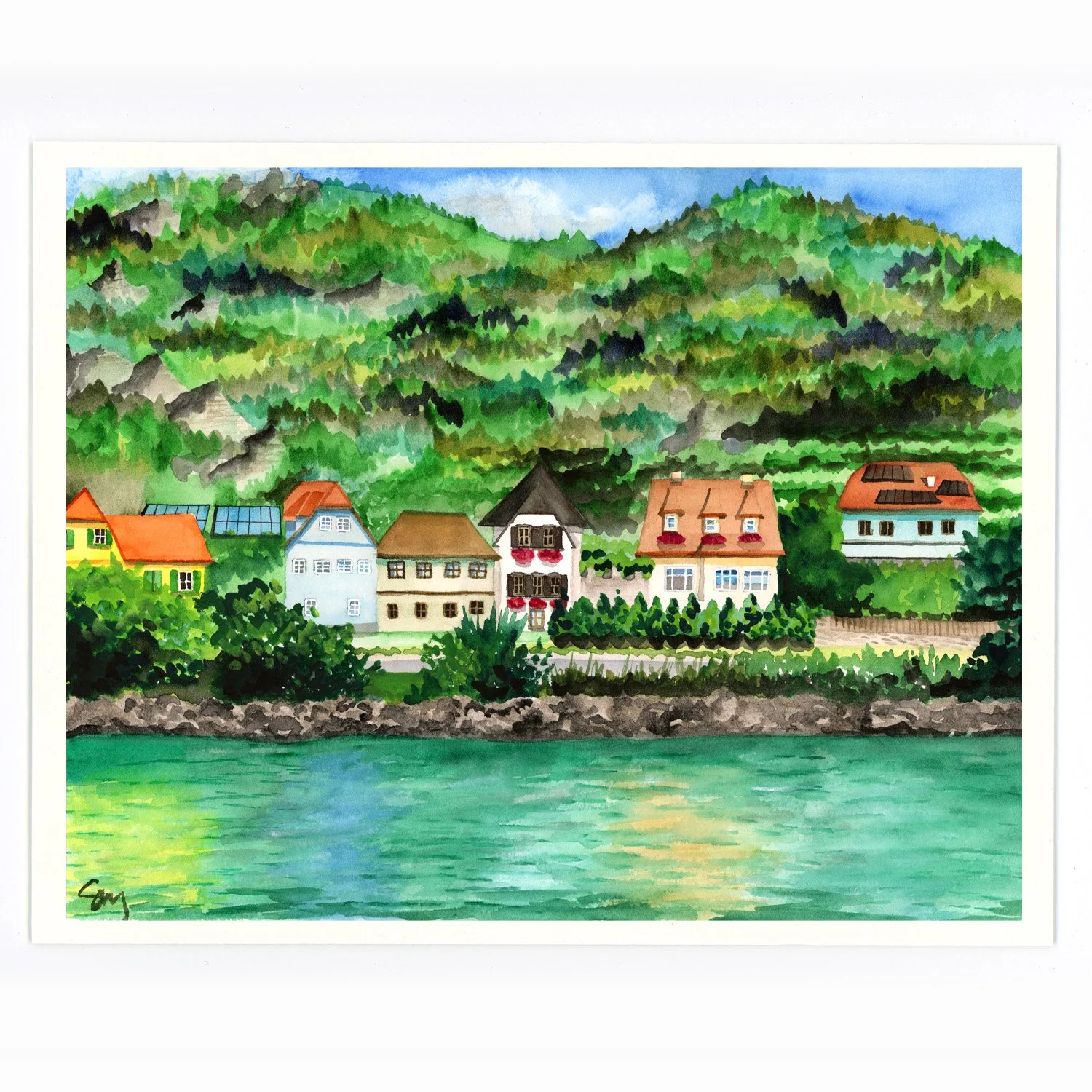 Waterfront scene of colorful houses along the shore, with lush green mountains in the background and a partly cloudy sky.
