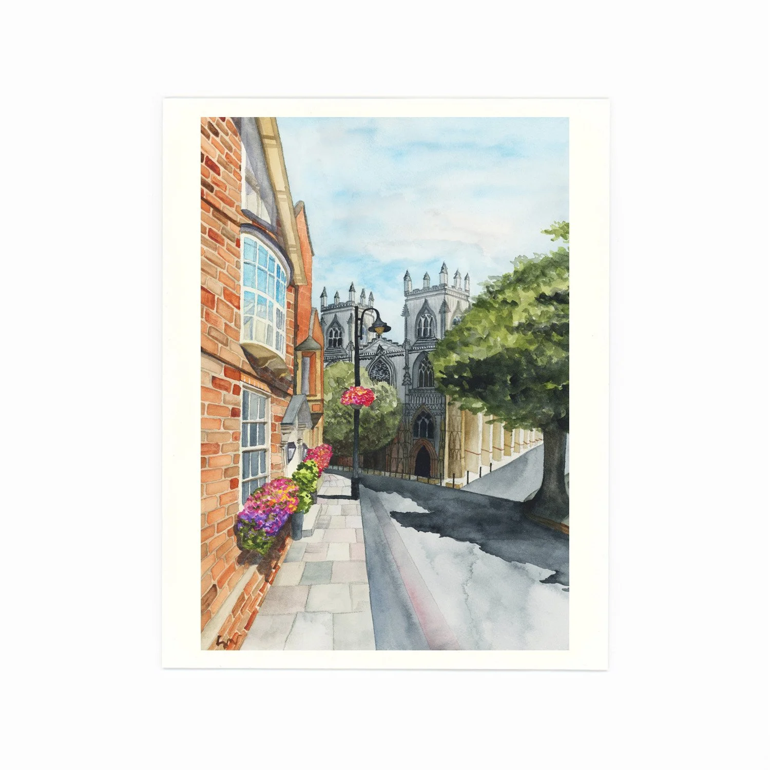A watercolor painting of a city street scene featuring brick and stone buildings, hanging flower baskets, a lamppost, and the distant façade of a gothic-style cathedral with towers and spires.