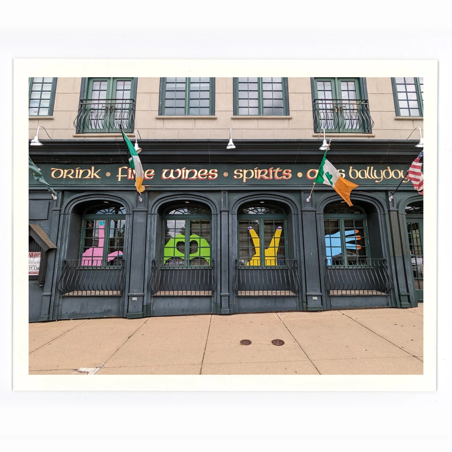 Front exterior of a pub with a black facade, rainbow flags, and windows with colorful cutouts spelling 'L', 'A', 'V', 'Y'.