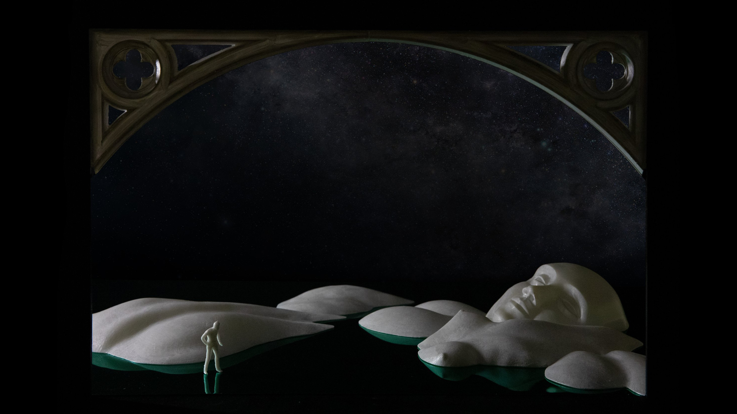 Sculpture of a human face and figure floating on water with an arch and night sky backdrop.