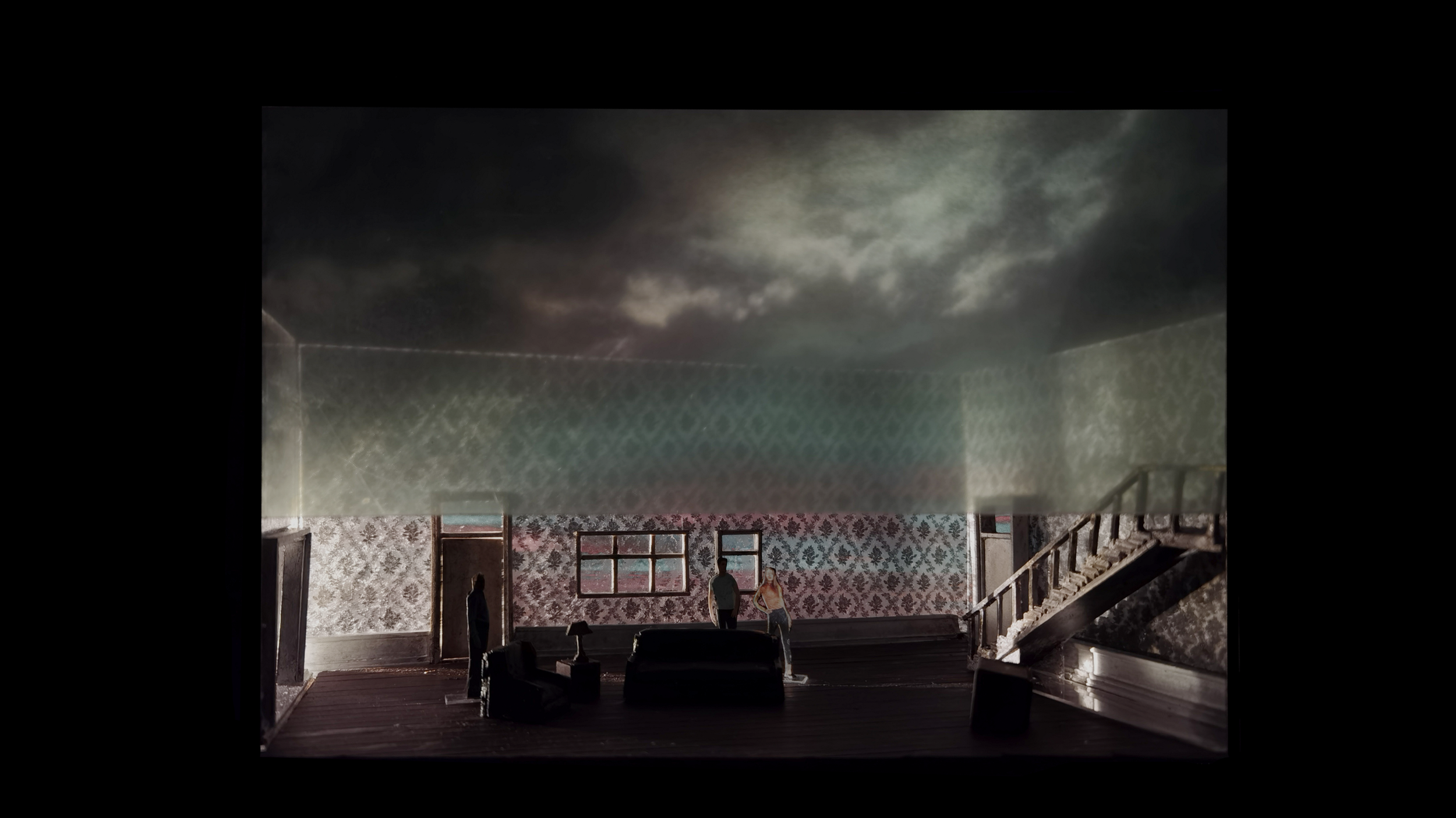 Dimly lit room with vintage wallpaper, a staircase, and two silhouetted figures. The room contains furniture, such as a sofa and table, and has windows with an eerie sky view.