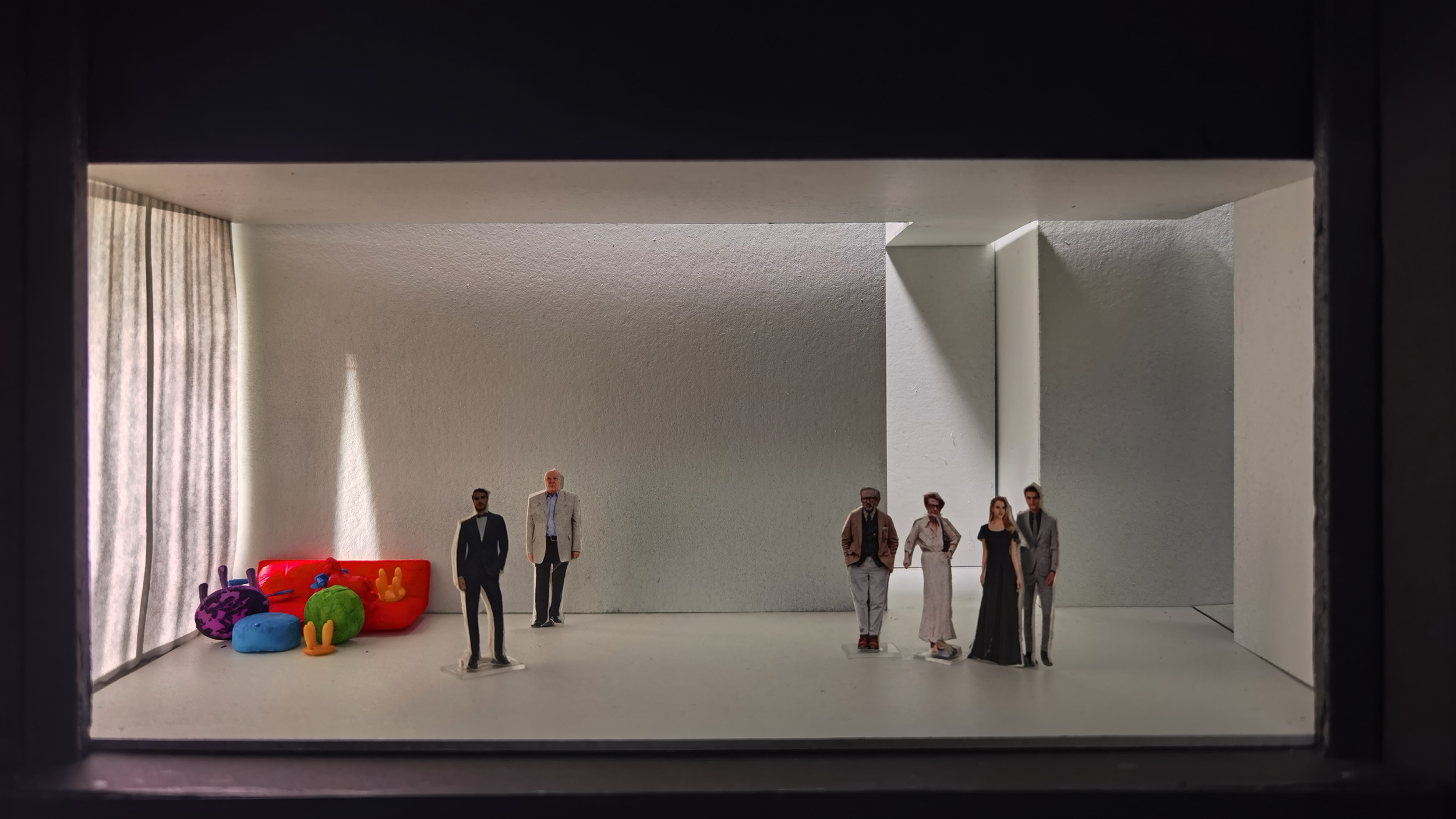 Miniature figures in a scale model room with colorful cushion-like objects and white curtains.