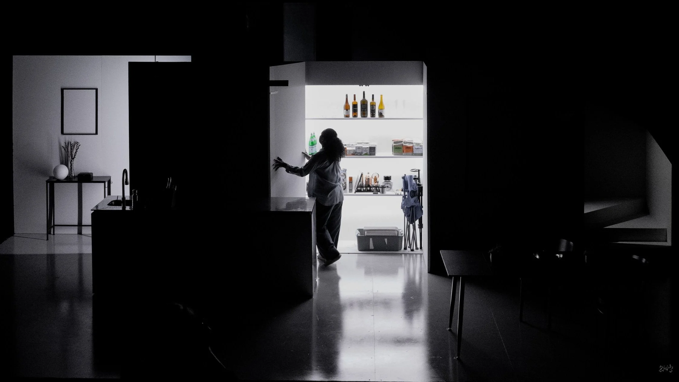 Silhouette of person in dimly lit kitchen, with open illuminated pantry, bottles, and kitchen items visible.