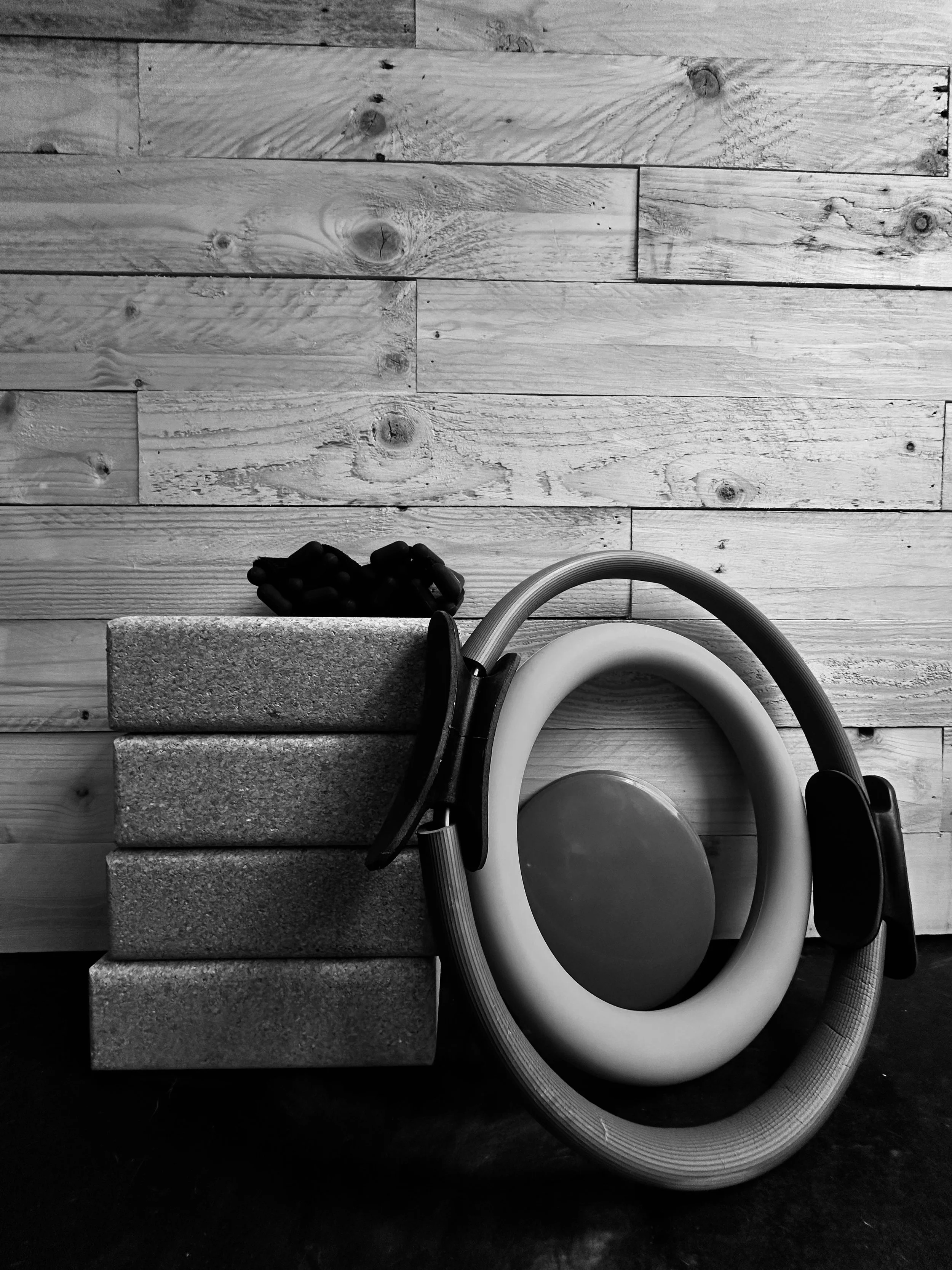 Black and white photo of a hardwood floor with a vacuum cleaner, a curled hose, three concrete blocks, and a partially visible mop.