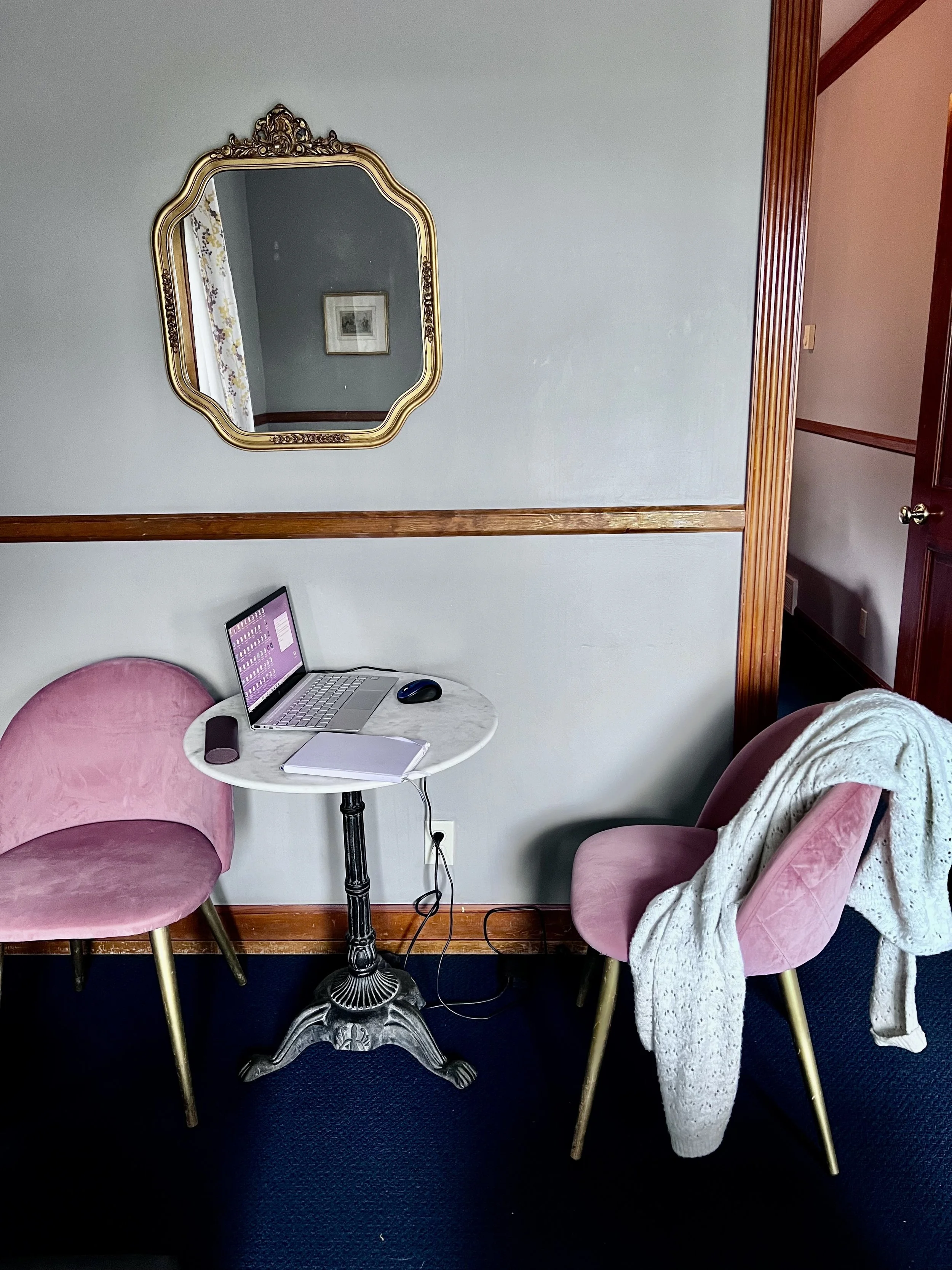 hotel room with two pick chairs and laptop on white table