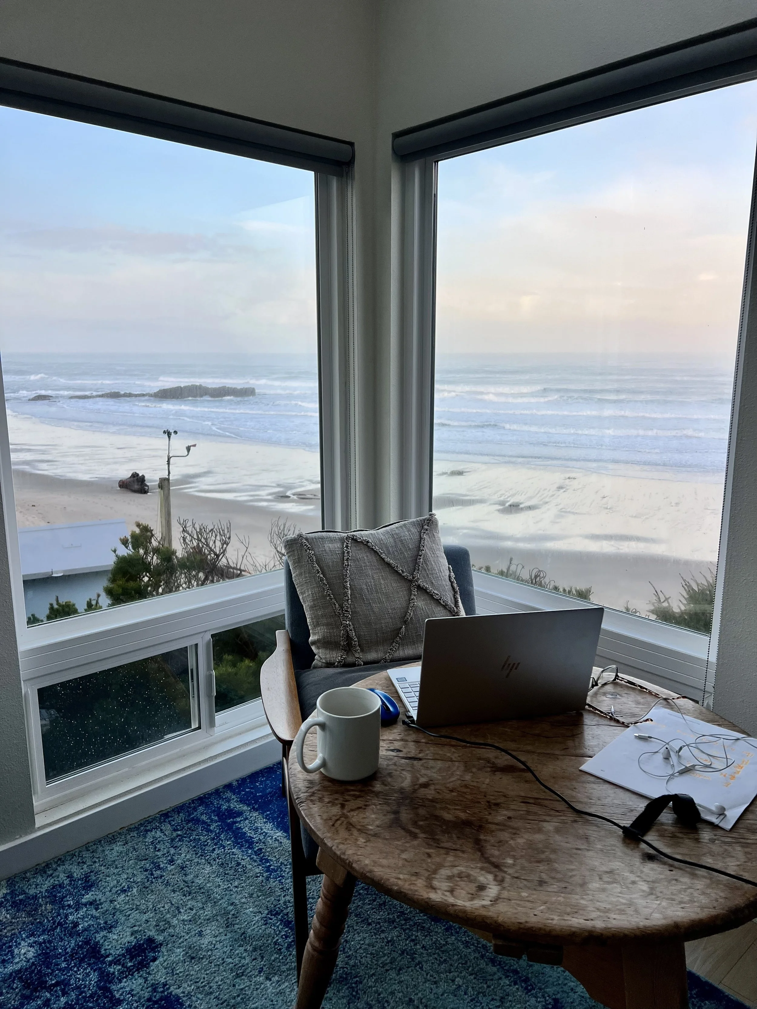 laptop open with sandy oceanview through window behind