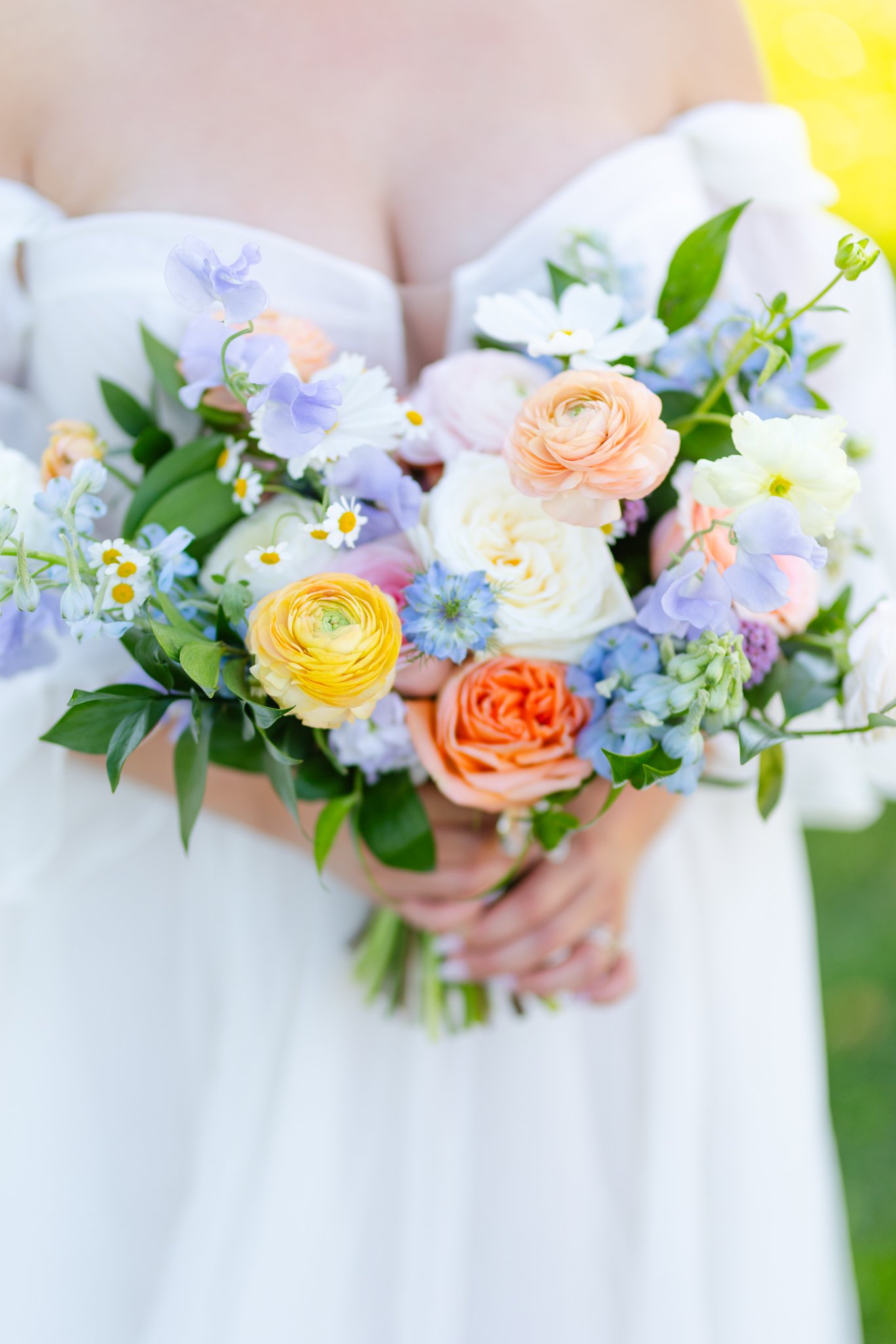 A person in a white dress holding a bouquet of colorful flowers, including peach, purple, white, and orange blooms with green leaves.
