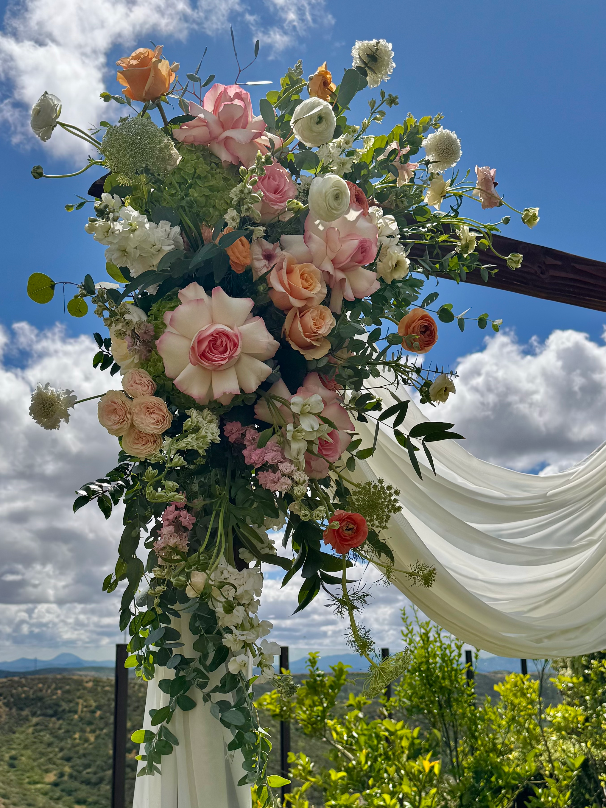 A colorful flower arrangement hanging outside against a partly cloudy sky and mountain landscape.