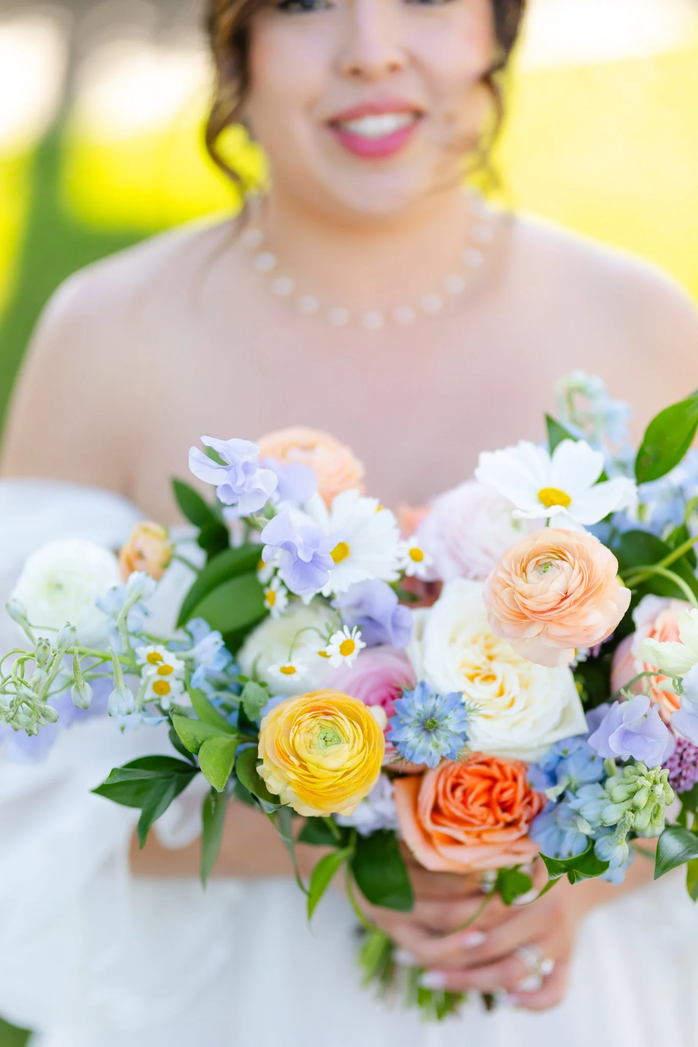 Wedding bouquet made of colorful blooms including roses, ranunculus, peonies, daisies, sweet peas, delphinium and other beautiful flowers. 