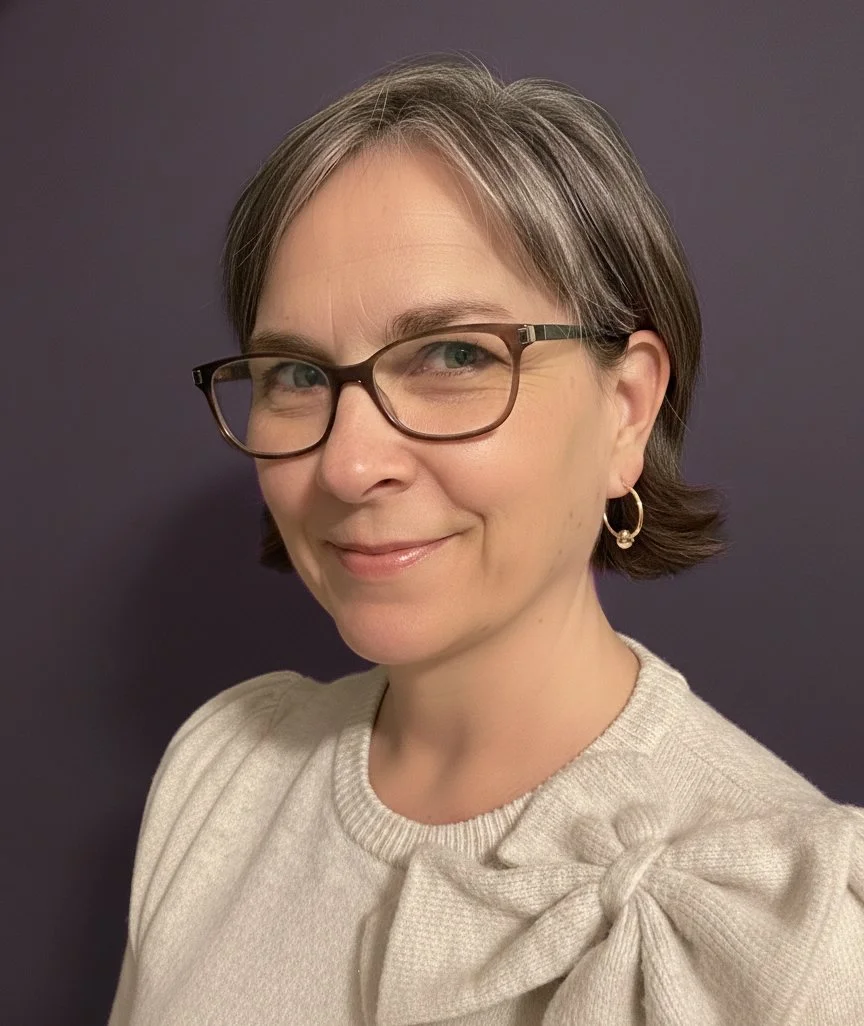 Woman with short hair, glasses, and hoop earrings smiling at the camera against a dark background.
