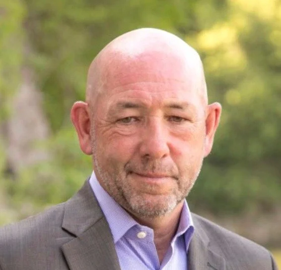 Man with a shaved head wearing a suit outdoors.