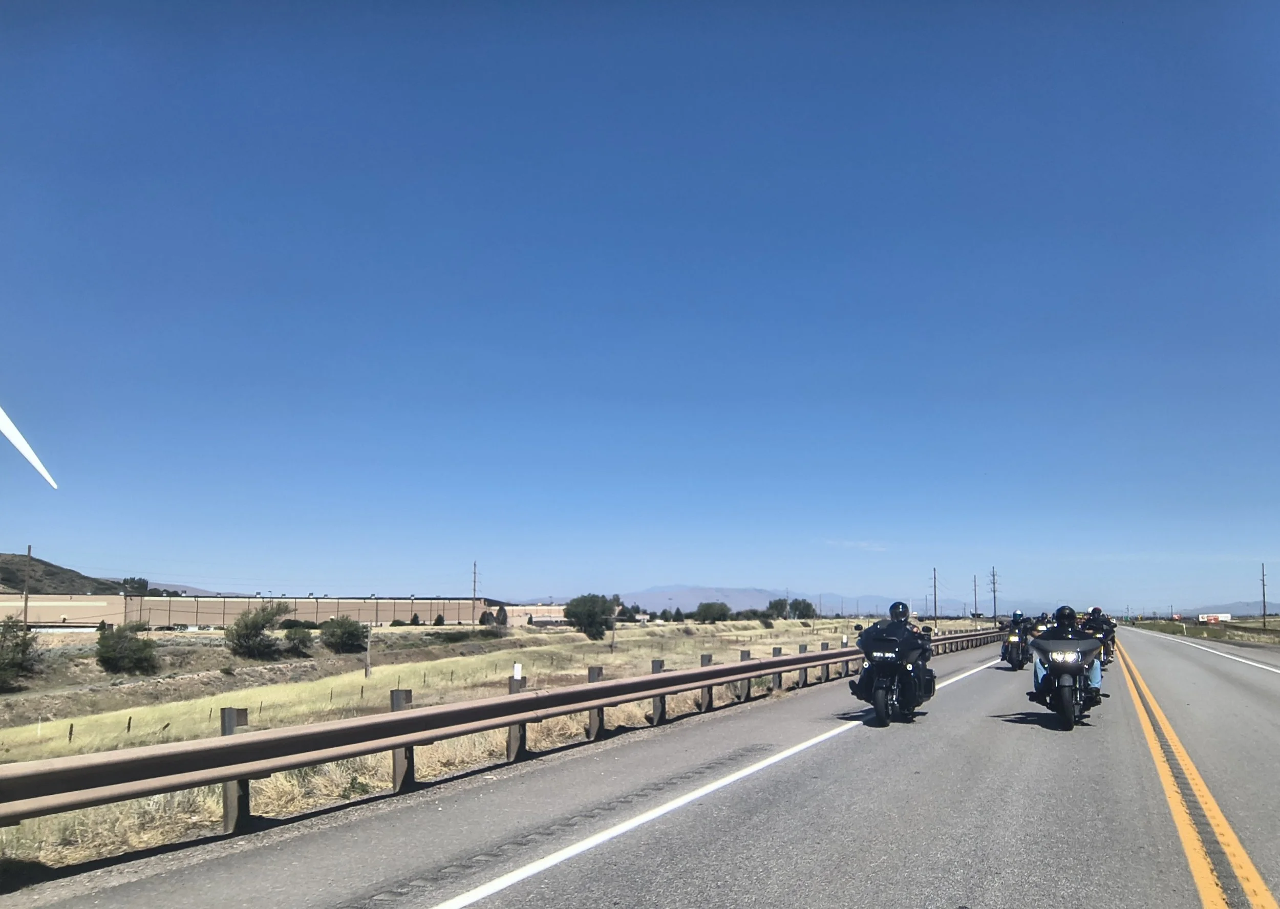 A group of motorcyclists riding on a highway through a desert landscape under a clear blue sky.
