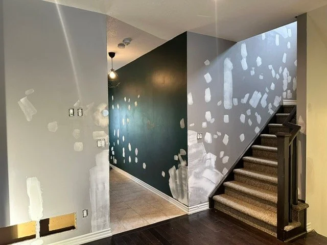 Interior of a home under renovation with drywall patches and unpainted walls, adjacent to carpeted stairs.
