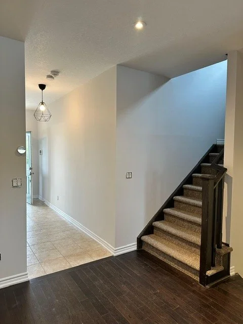 Empty hallway and staircase in a modern house interior with beige walls, dark wood stairs, and a tiled floor.
