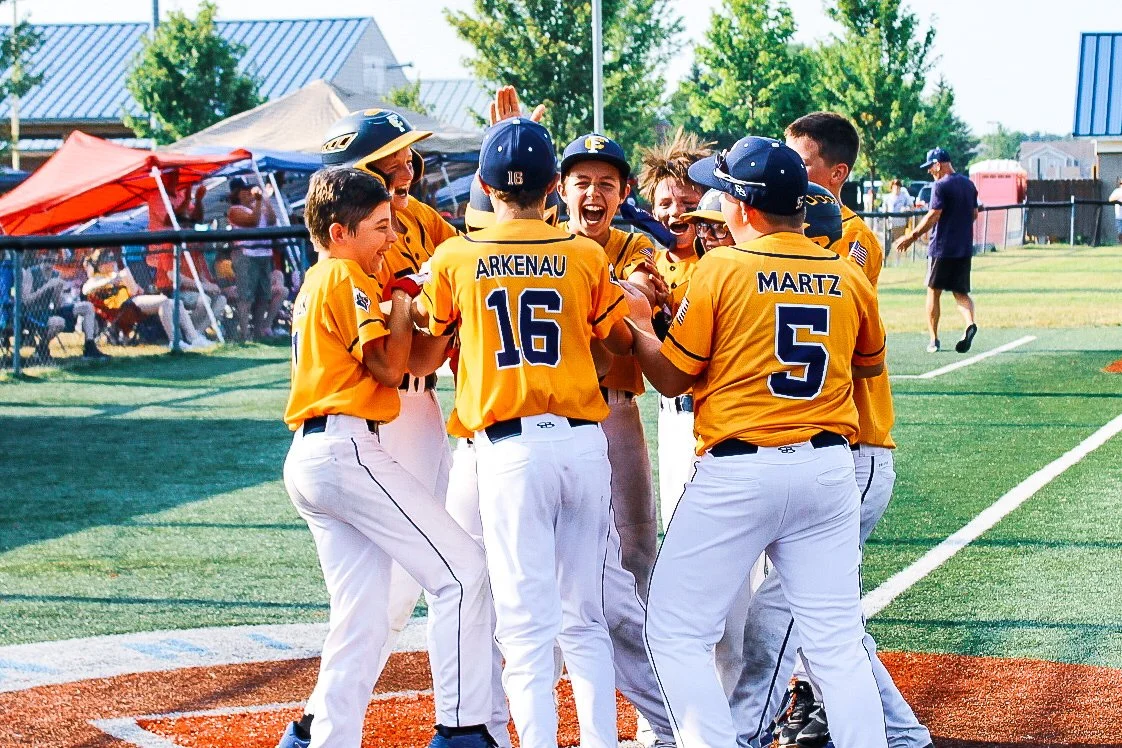 Youth baseball team in yellow jerseys celebrating a home run together on the field.