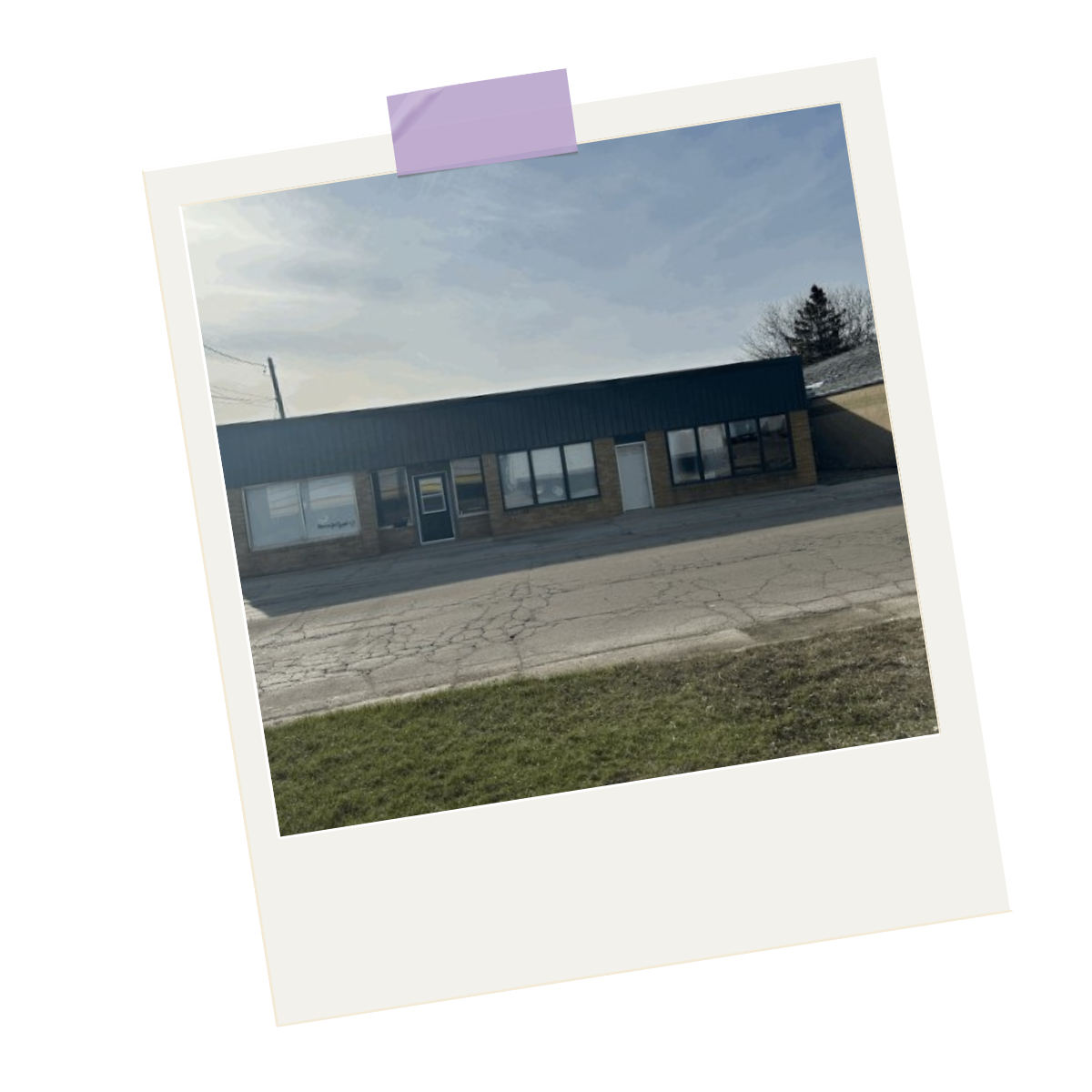 A single-story commercial building with large front windows, a dark-colored metal roof, and a brick facade in a small town or suburban area.