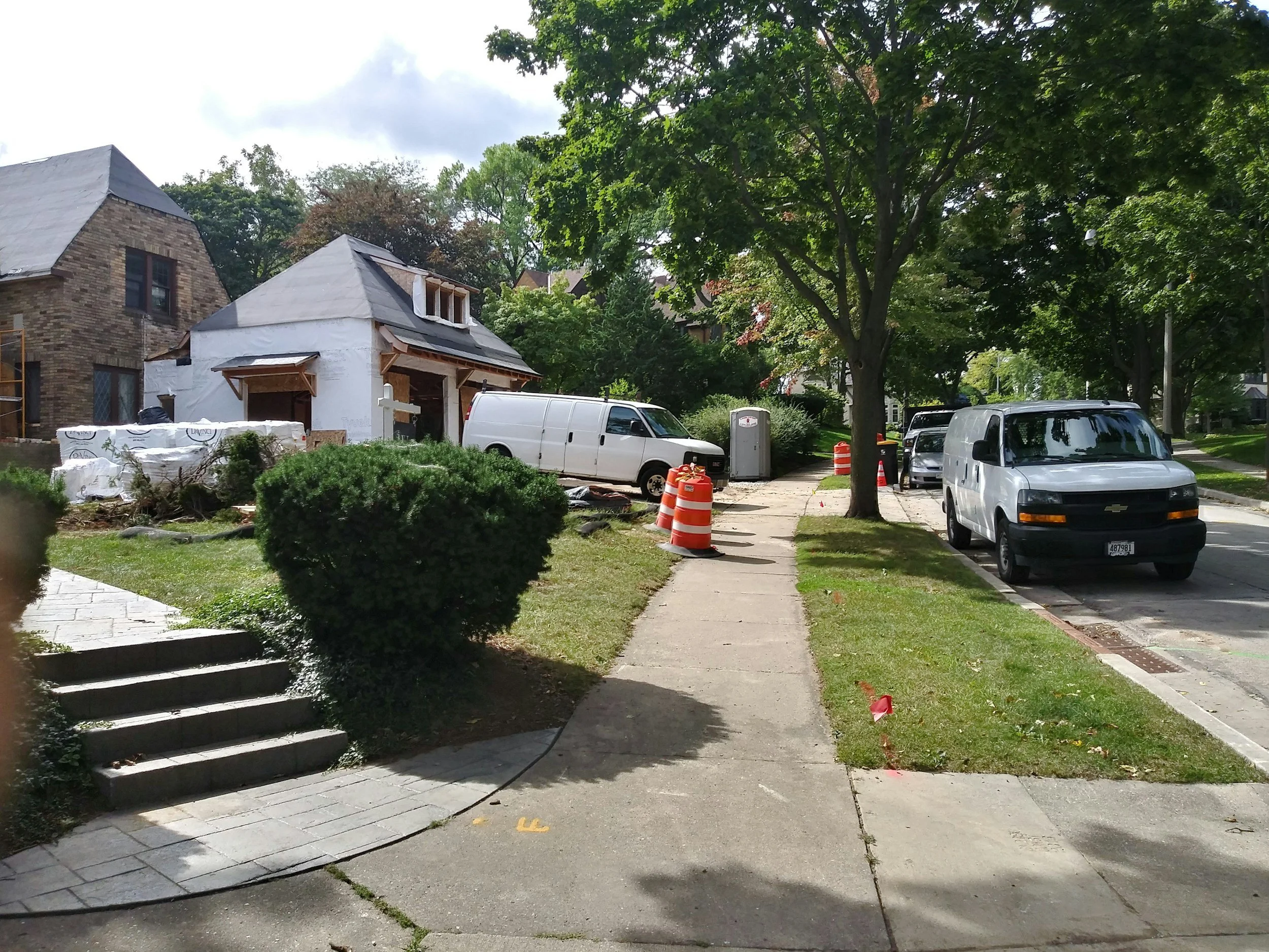Street view with houses under construction, construction cones, parked vans, and trees.