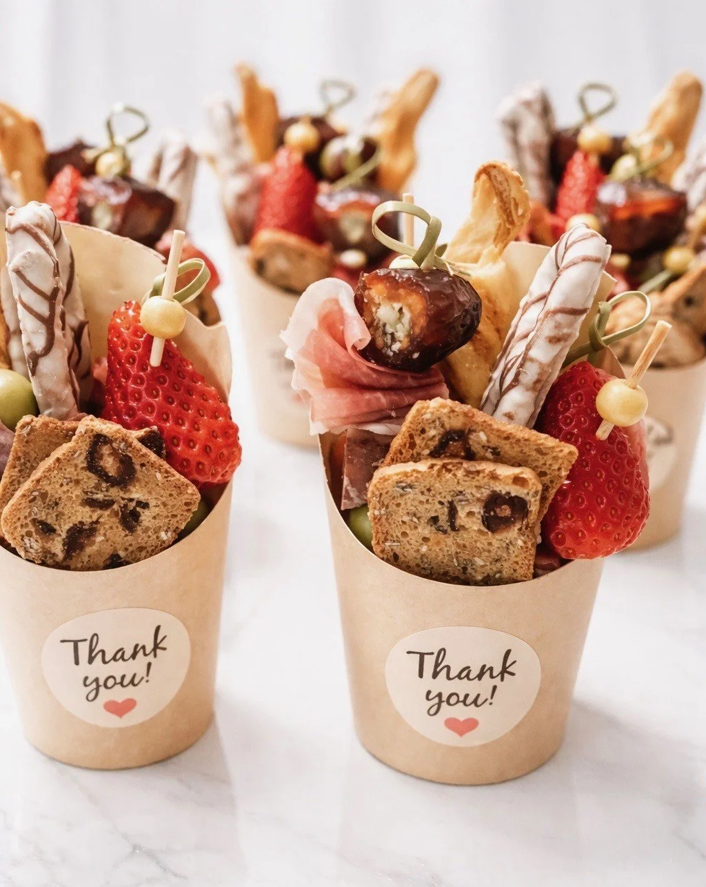 Sweet dessert cups filled with cookies, strawberries, grapes, chocolate-covered treats, and decorative cookies, with 'Thank you!' stickers on the cups.