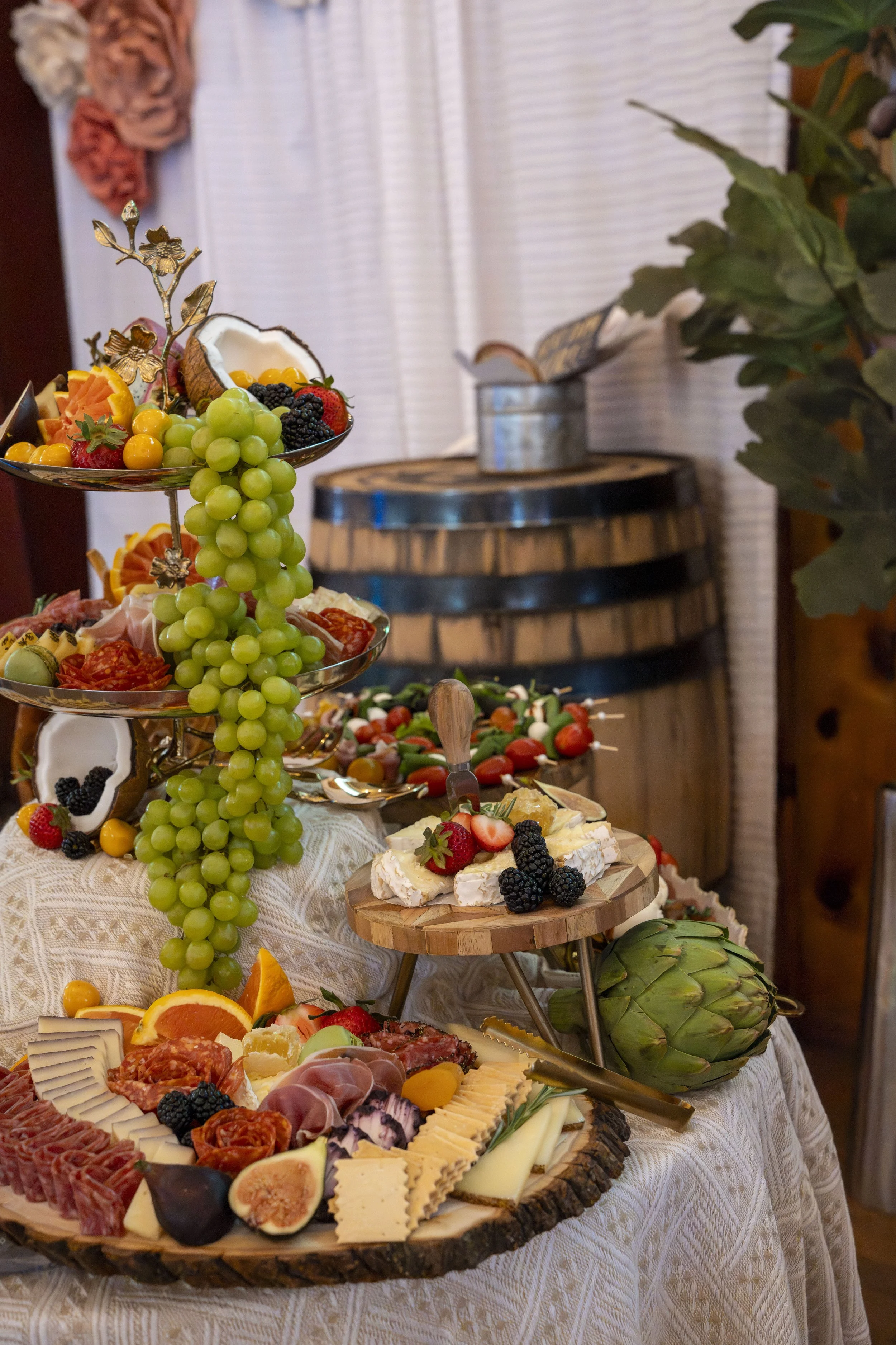 Plate with assorted cheeses, meats, fruits, and vegetables, including grapes, strawberries, blackberries, figs, and sliced oranges, arranged on a rustic wooden platter on a table with a patterned tablecloth.
