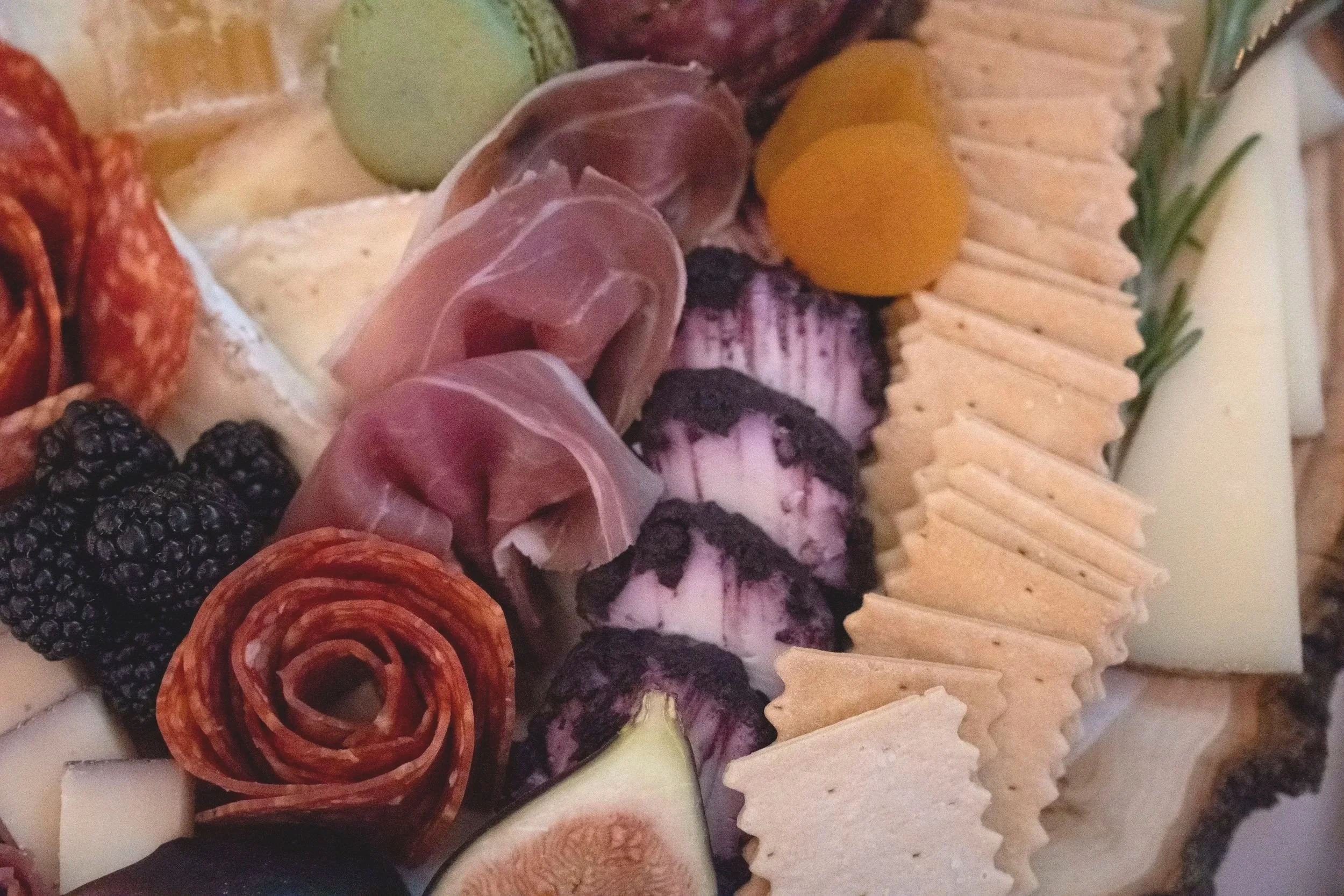 Close-up of a cheese and meat platter with crackers, grapes, blackberries, and rolled cured meats.