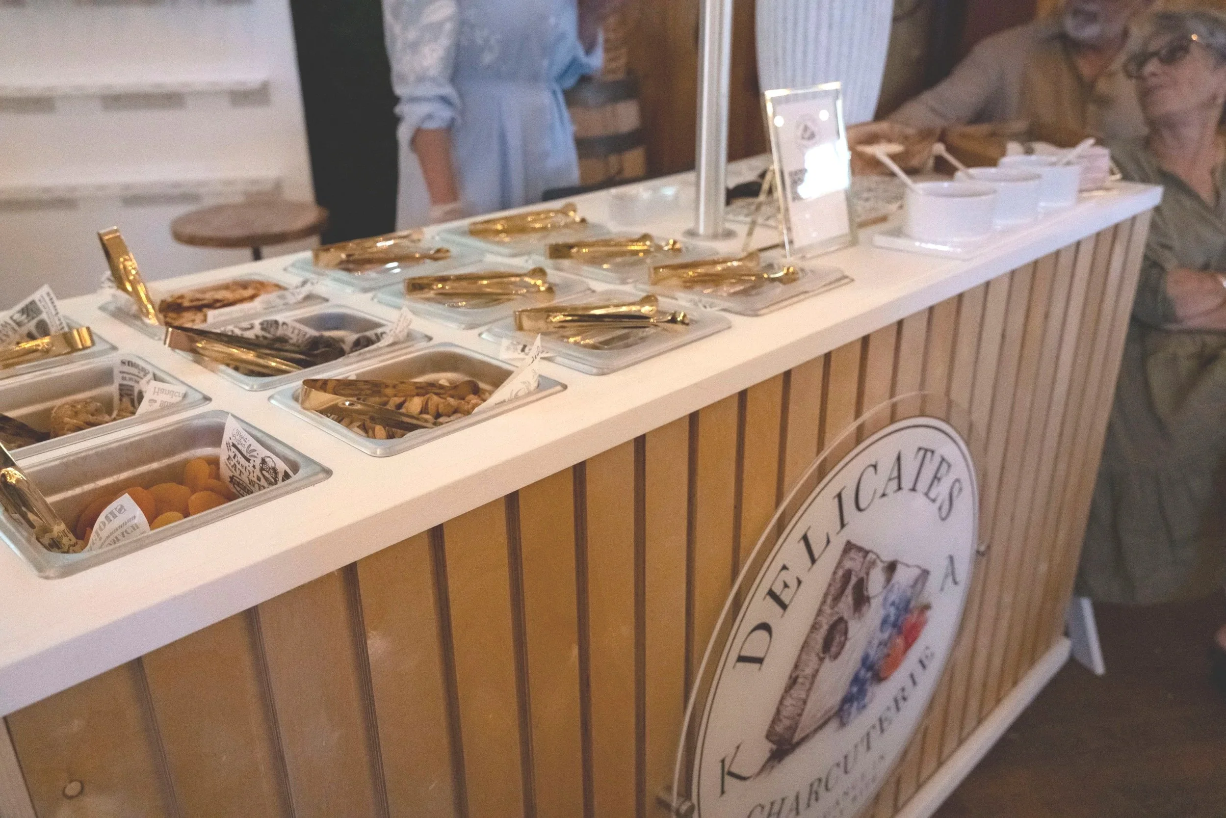 A display table with various containers filled with different types of snacks, possibly at a food tasting event, with a sign in the background.