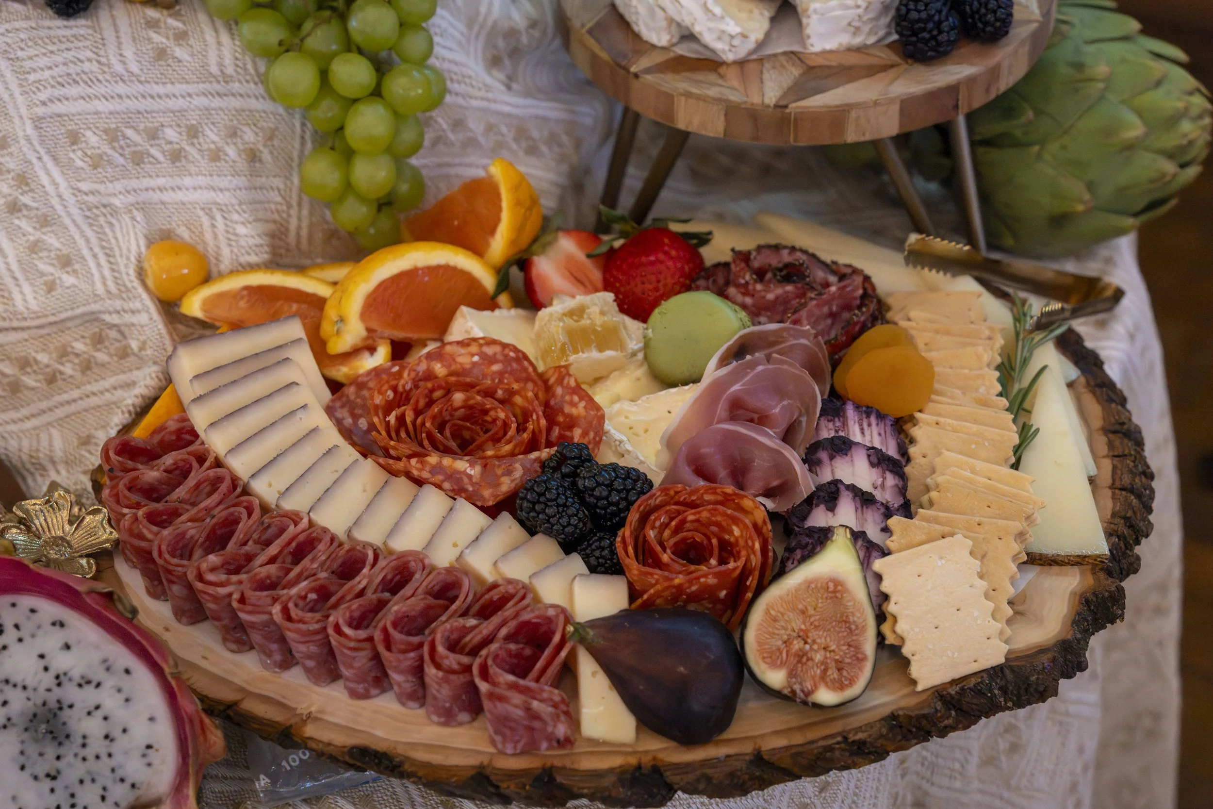 A cheese and charcuterie platter featuring various cheeses, cured meats, fresh strawberries, figs, blackberries, grapes, oranges, and other fruits, arranged on a wooden serving board.