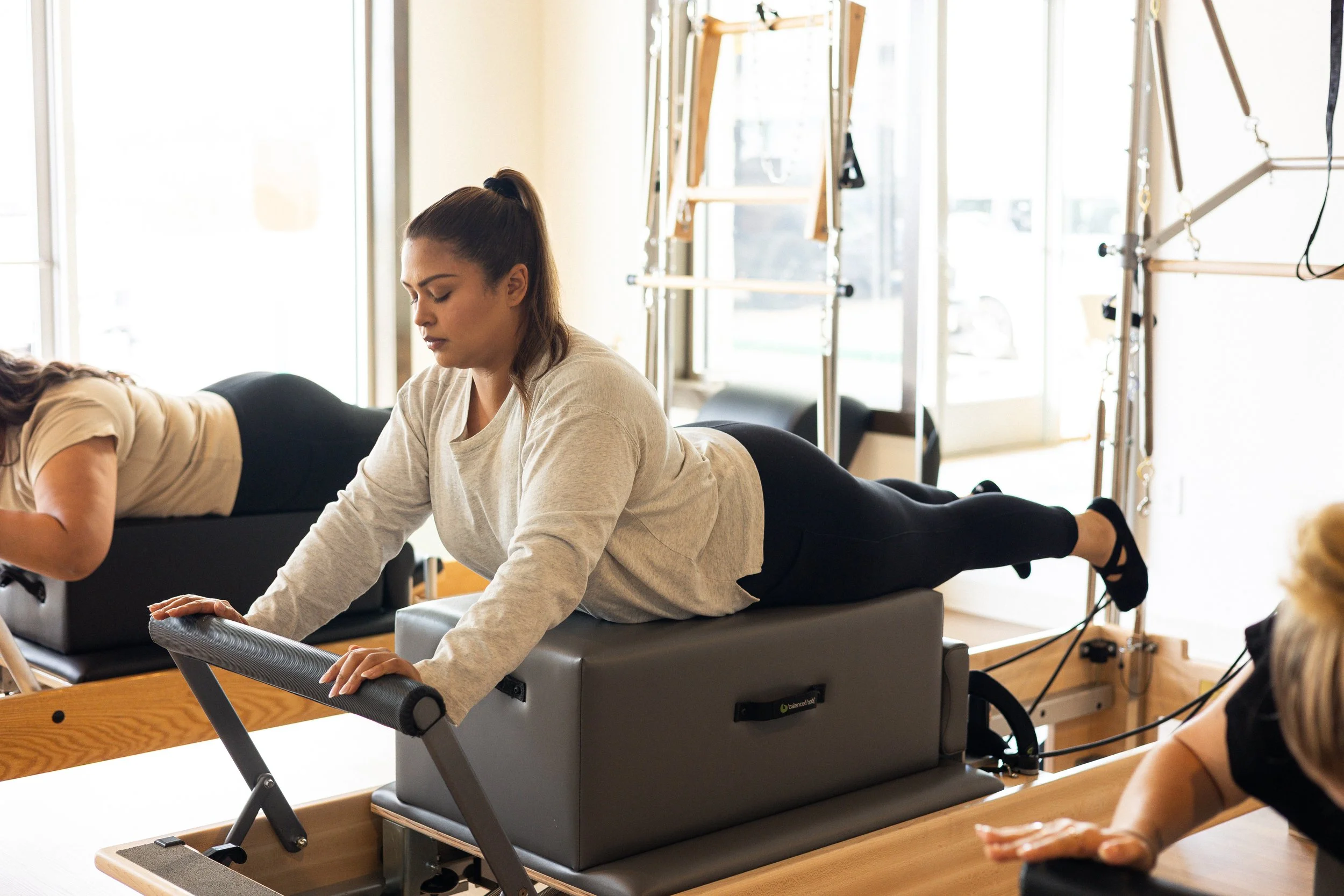 Woman performing Pilates exercise on a reformer machine in a fitness studio with natural light.