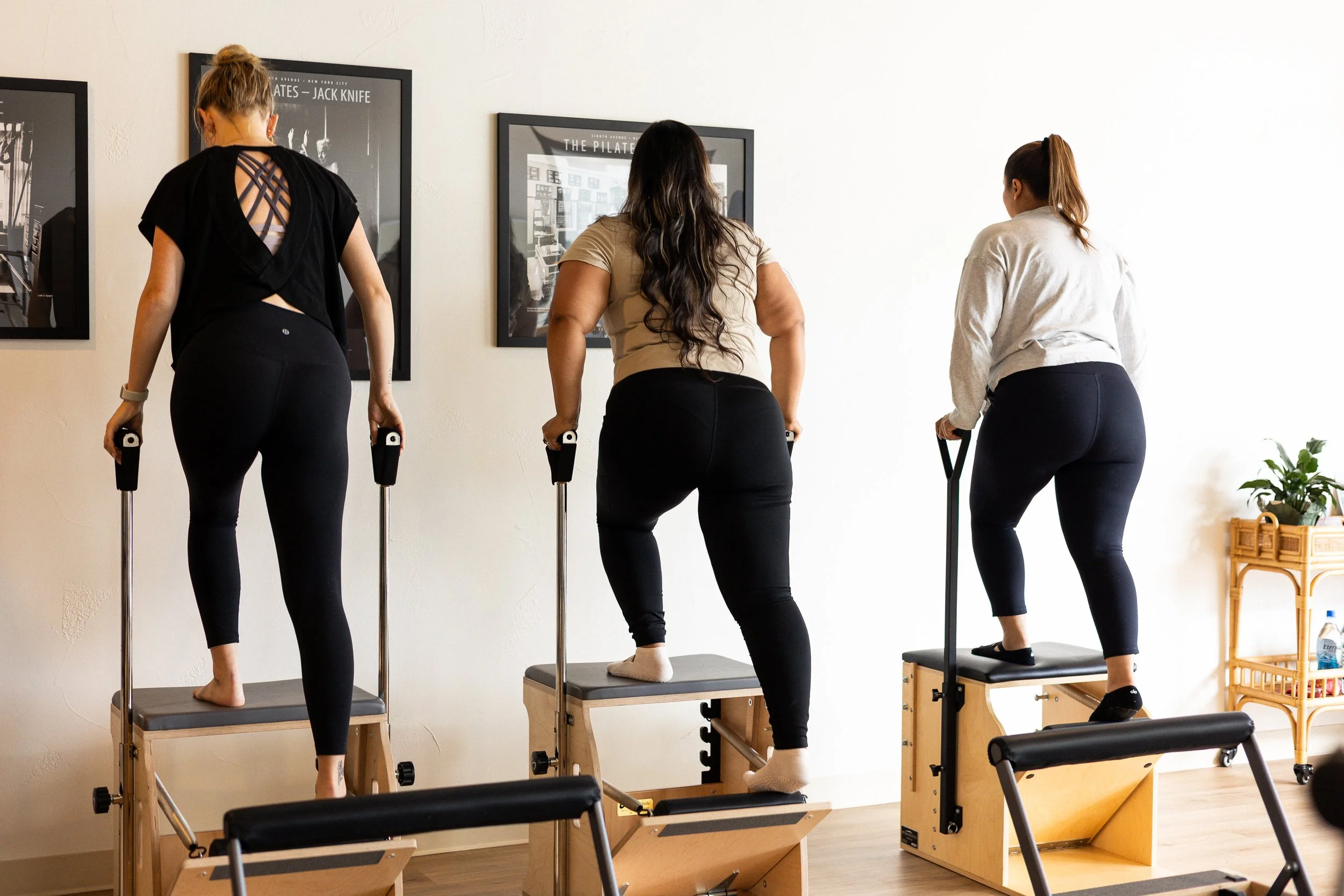 Three women exercising on pilates reformer machines in a fitness studio, viewed from the back.