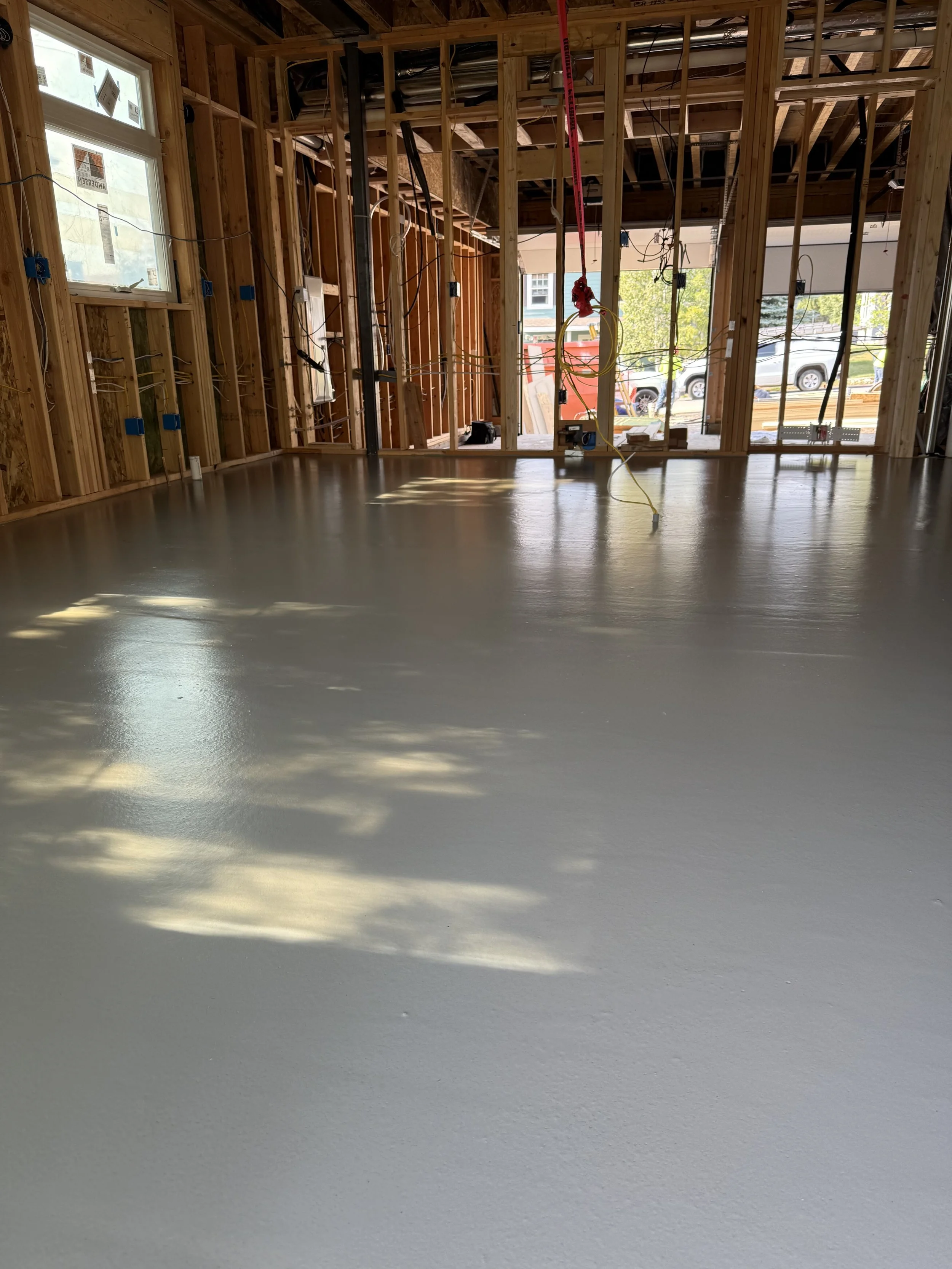 Interior of a house under construction with a freshly poured concrete floor and exposed wooden framing.