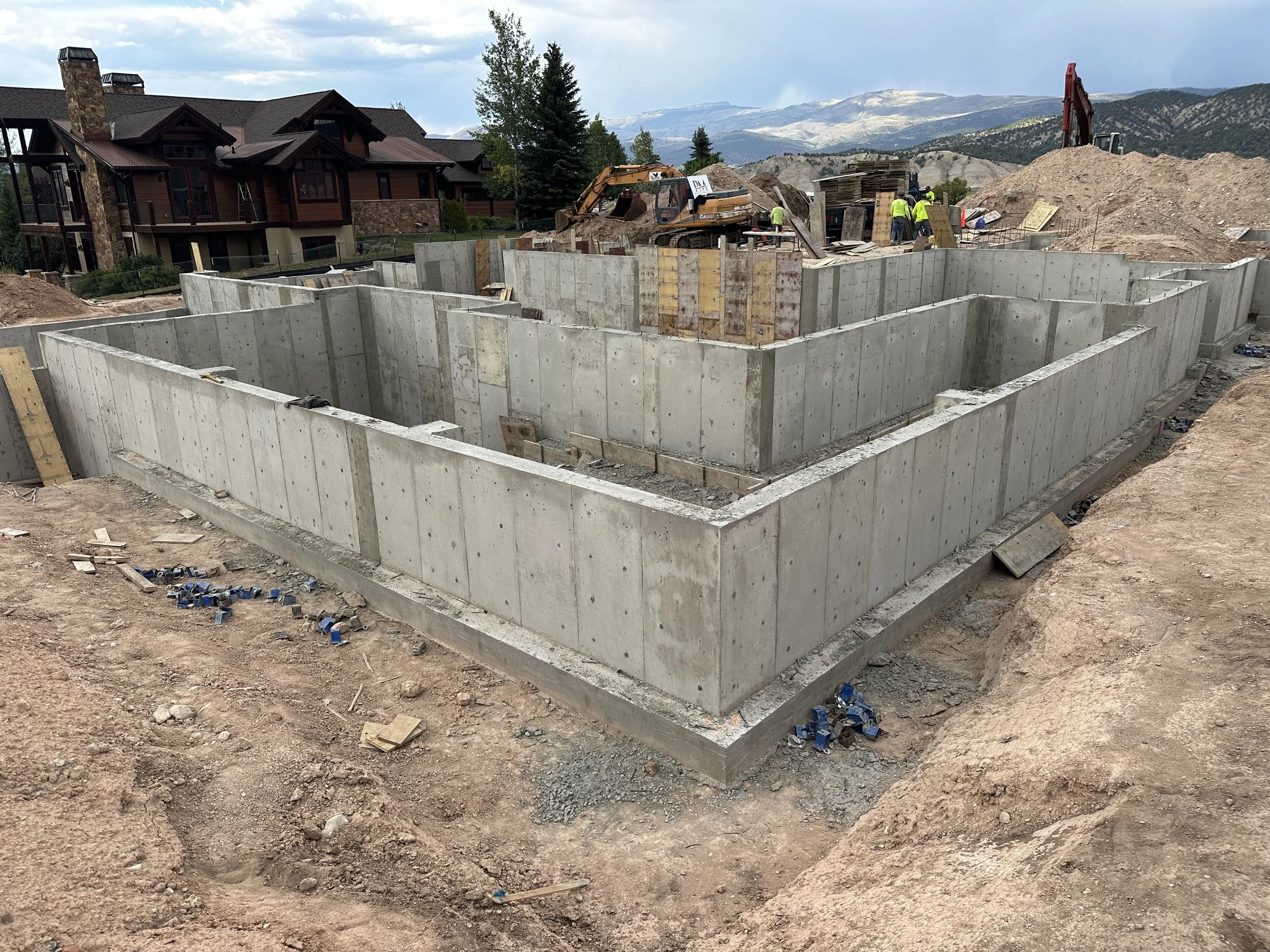 Concrete foundation at a construction site with workers and excavators, mountainous landscape in the background.