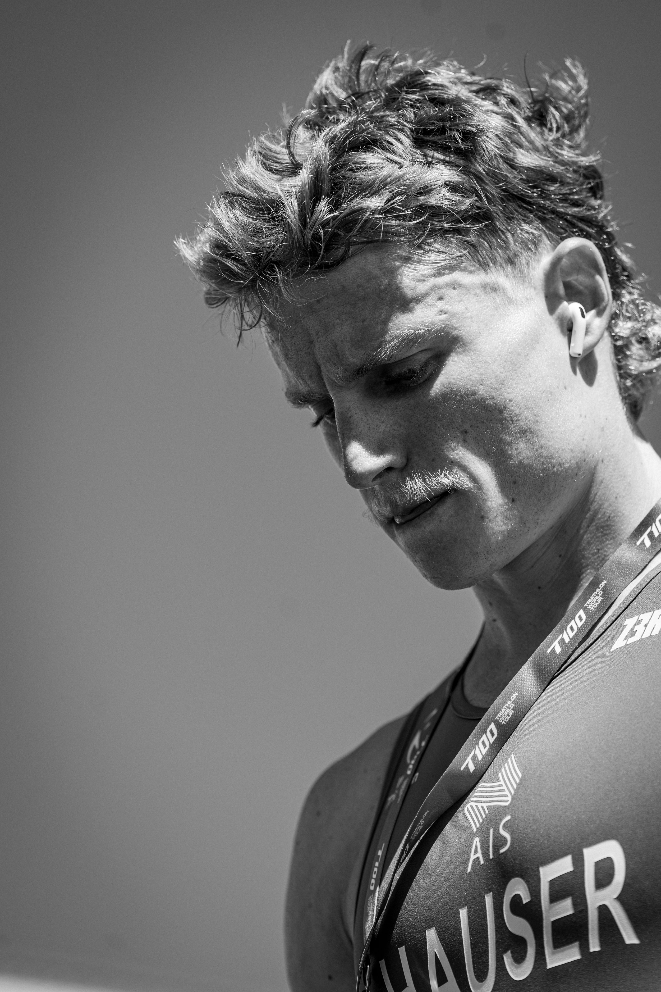 Portrait d'un athlète avec un look de cheveux frisés et portant une médaille, en noir et blanc.