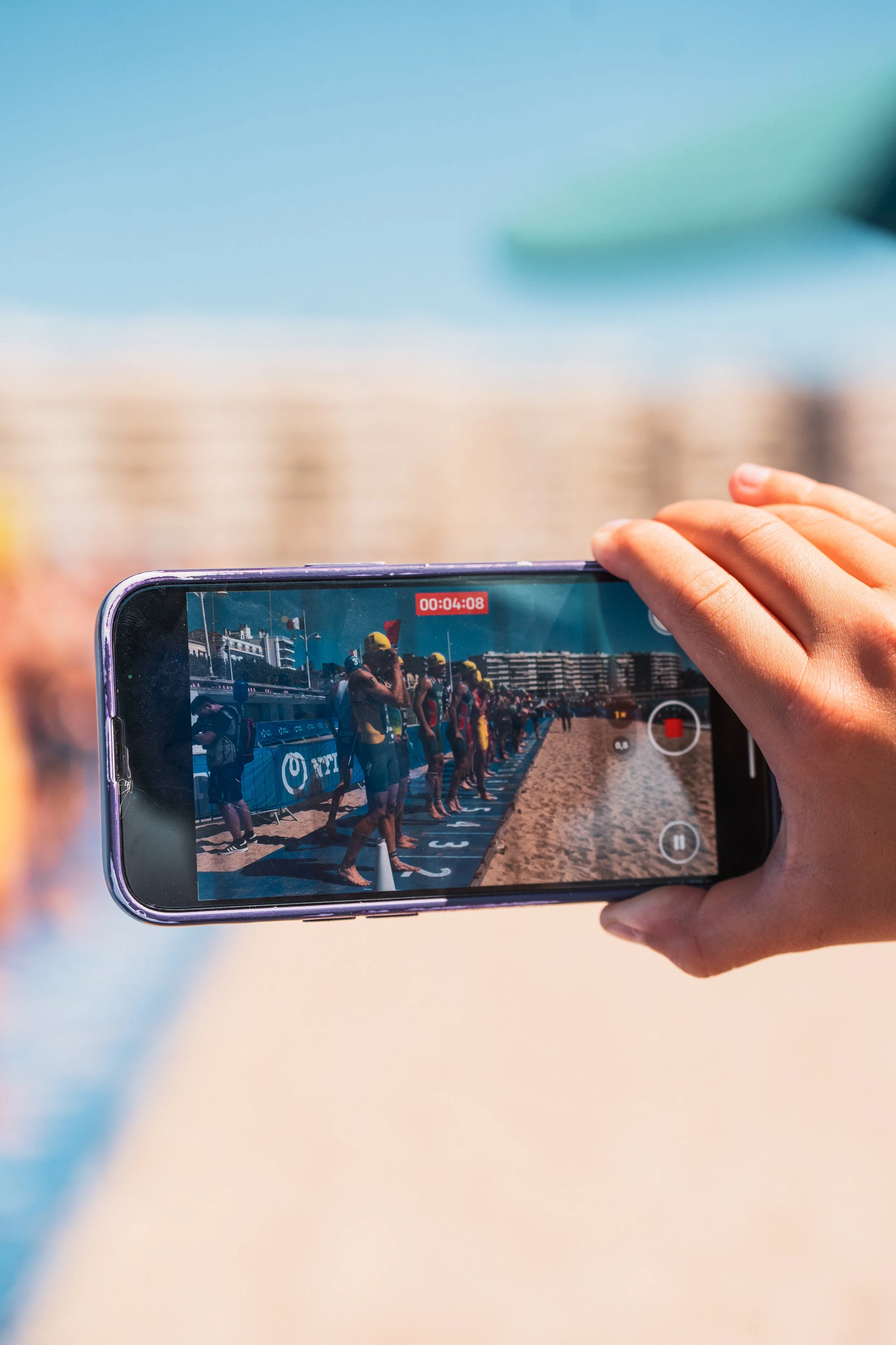 Une personne tient un téléphone prenant une photo ou une vidéo de nageurs en ligne sur la plage.