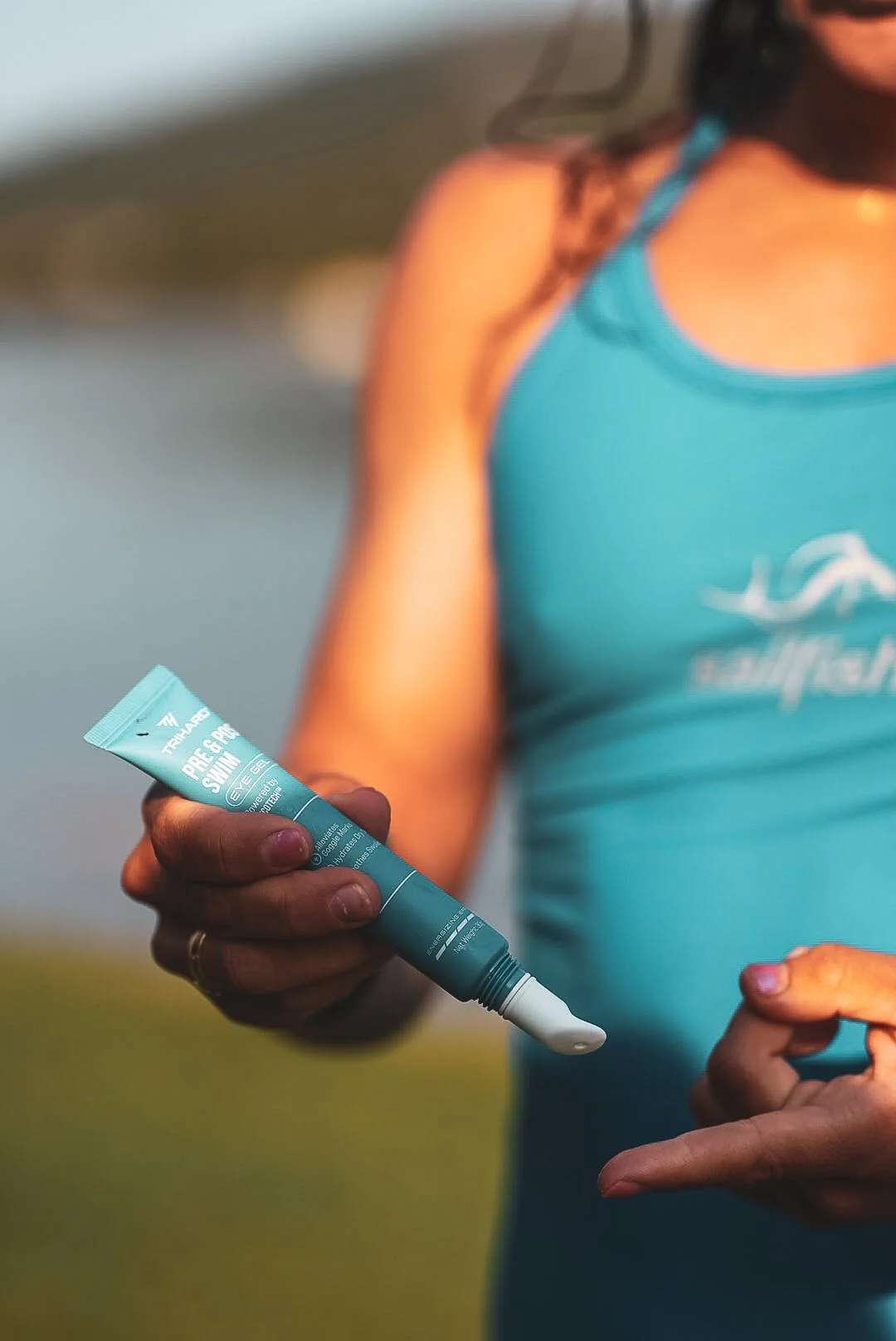 Une femme portant un débardeur bleu tiens un tube de crème solaire avec la mention "PRE- & POST SWIM" et une écriture en français.