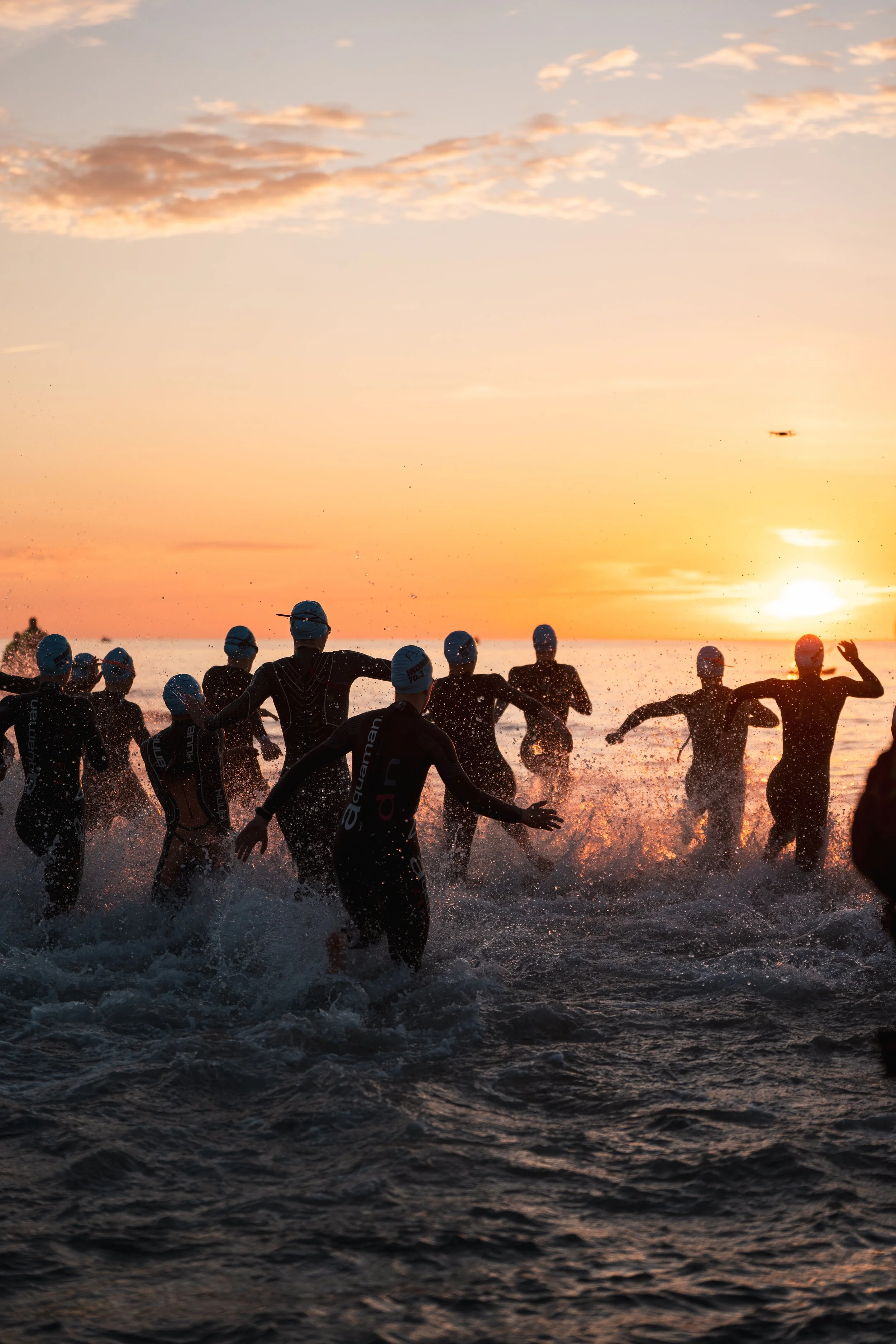 Groupe de nageurs participant à un triathlon à la tombée de la nuit, esquissant des mouvements dans l'eau avec un ciel coloré en fond.