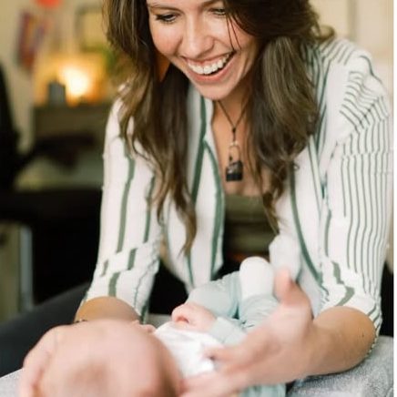 A woman smiling and holding a newborn baby in her arms.