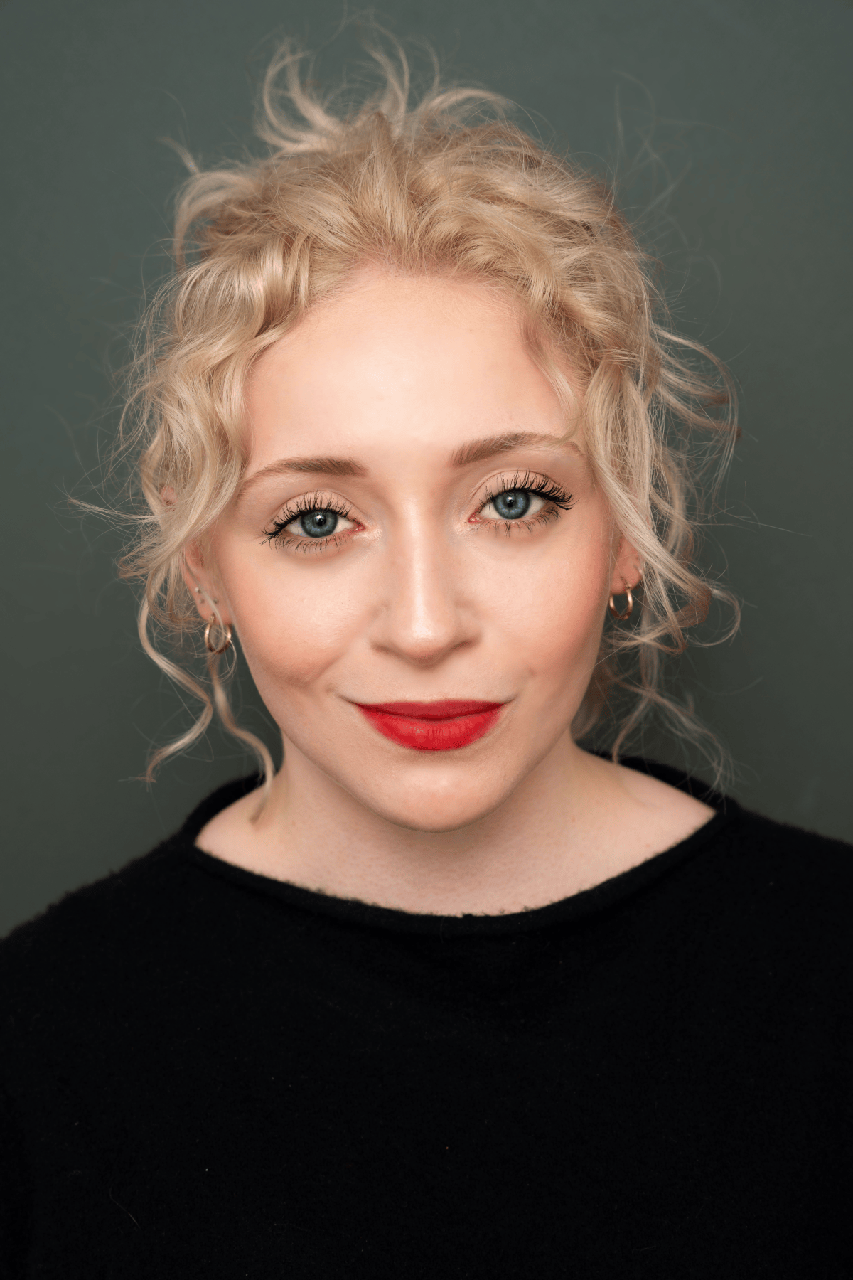 Photo of actress Mara Jade Koenig with blonde curly hair up in a bun, wearing a black shirt.