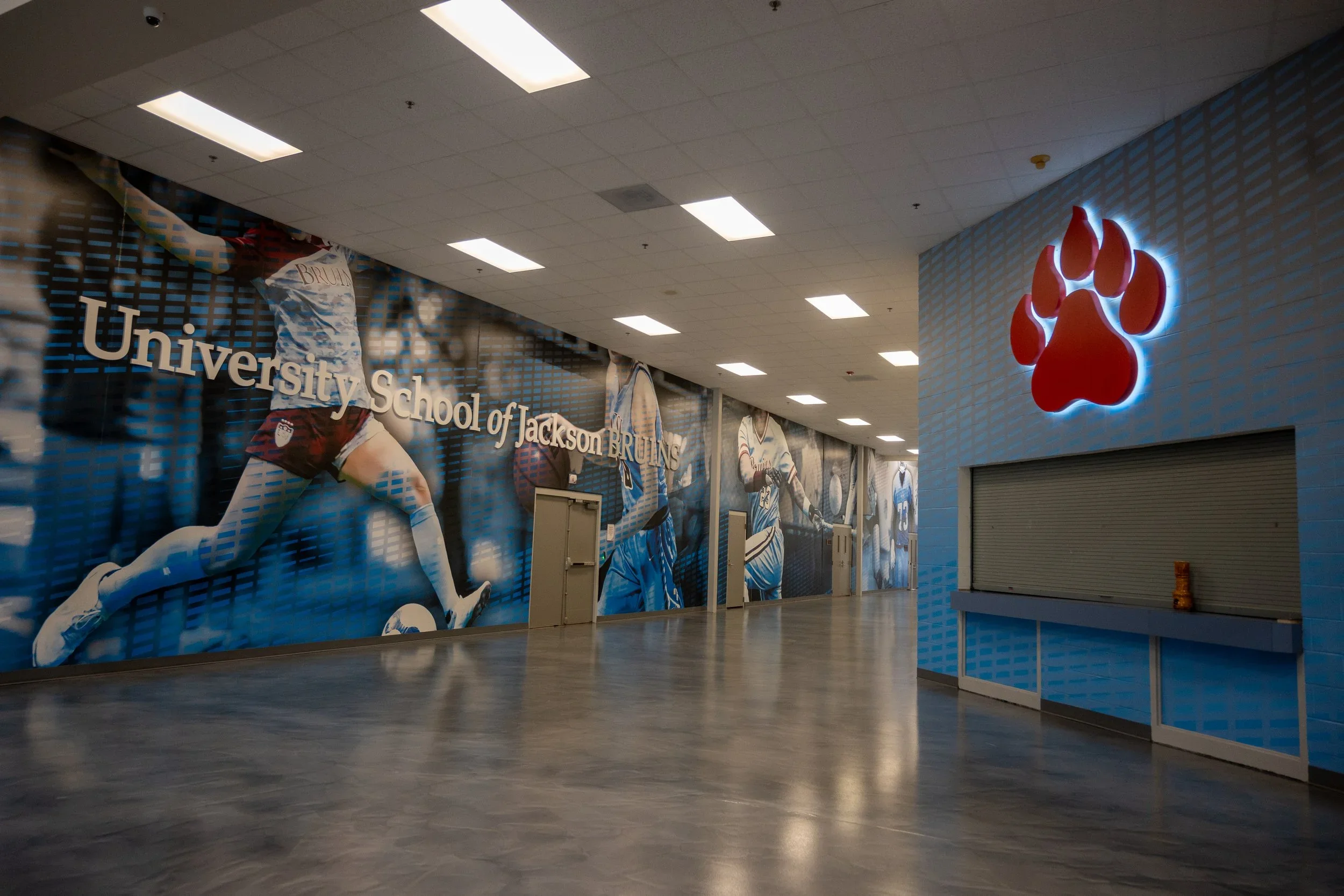Interior view of Clemson University football venue with a large mural of football players and a bright illuminated paw print logo on the wall.