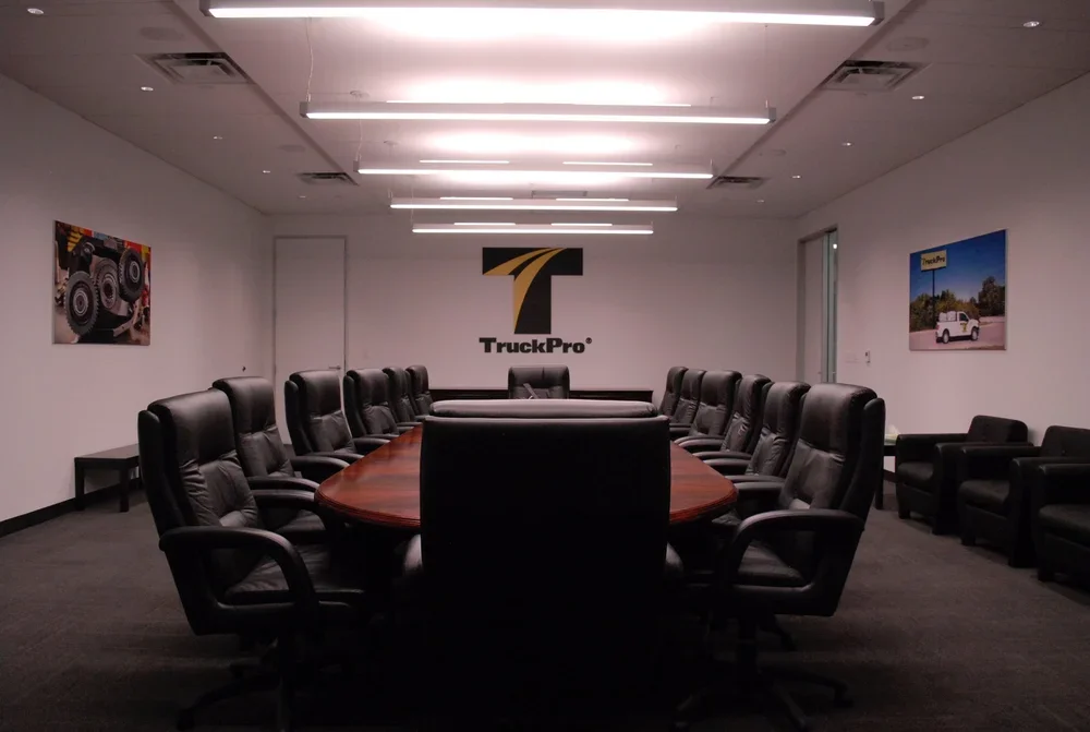 Empty conference room with a large oval table surrounded by black office chairs, featuring a TruckPro logo on the wall.