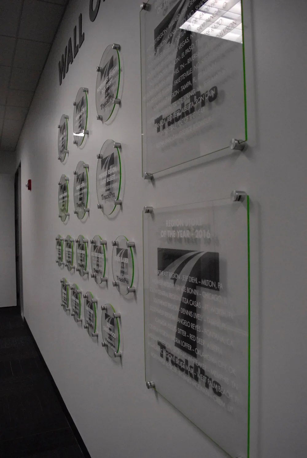 Wall display with multiple awards and plaques, including regional awards for Best Fleet and Region of the Year, mounted on a white wall in an office or corporate setting.
