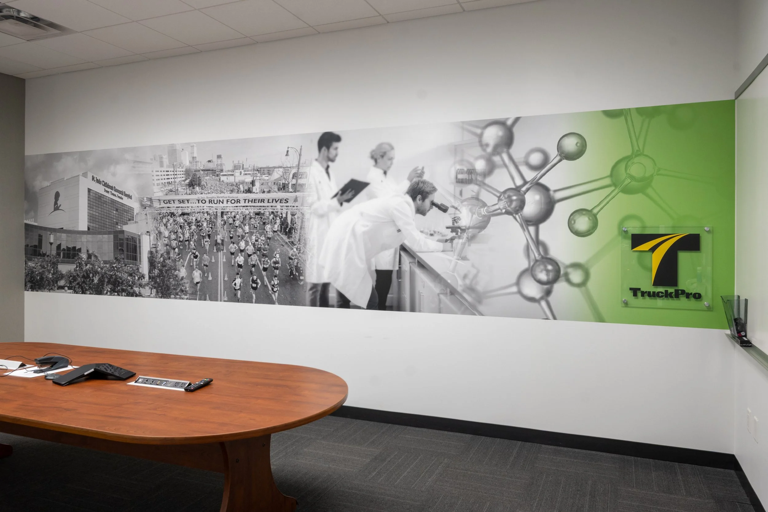 Office wall mural showing scientists working in a lab, a cityscape, and a crowd of runners, with a green abstract molecular structure and a TruckPro logo.