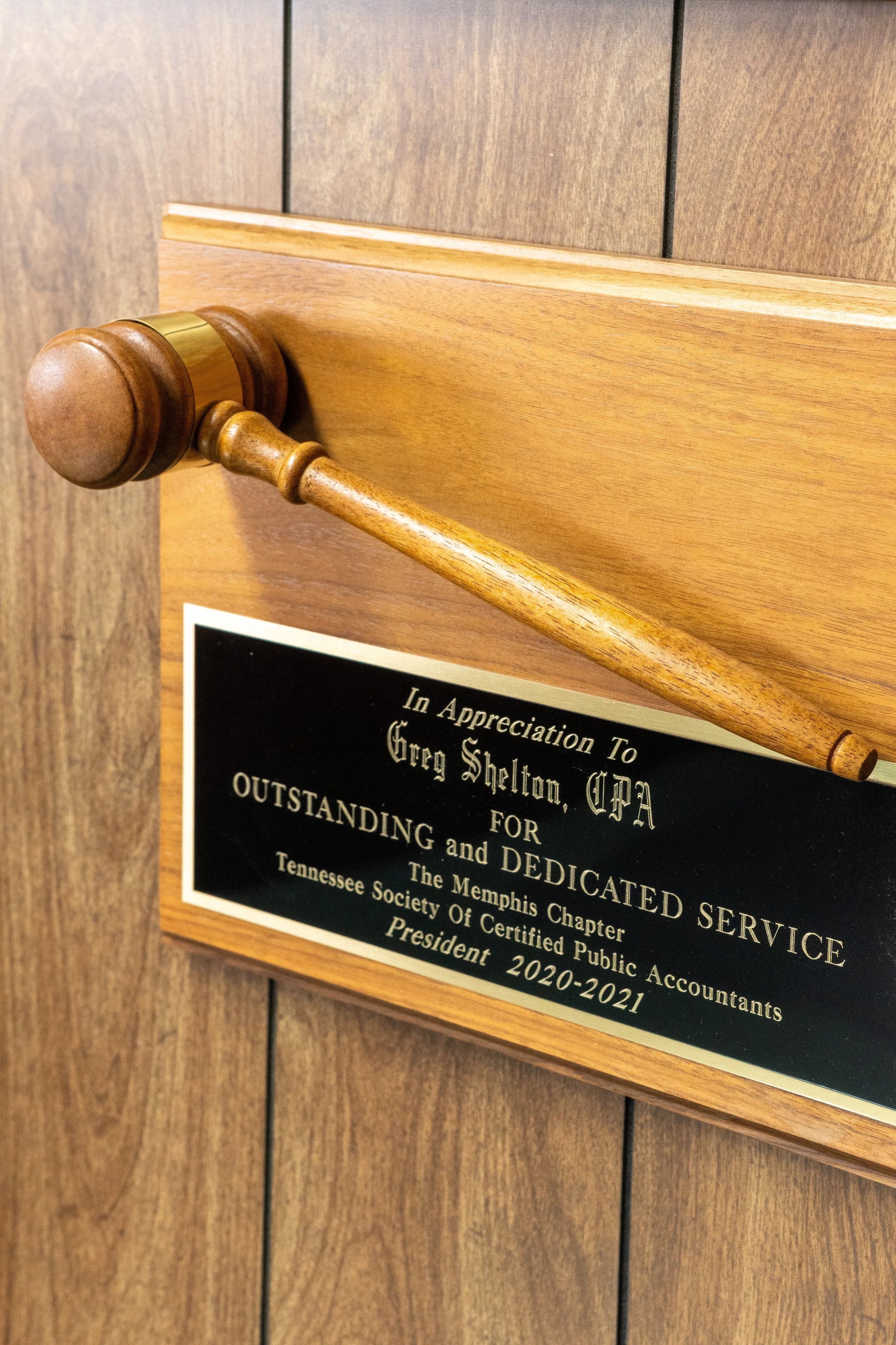 Plaque on a wooden wall honoring Greg Shelton, CPA, for outstanding service and dedication during his term as president of the Memphis Chapter of the Tennessee Society of Certified Public Accountants from 2020 to 2021.
