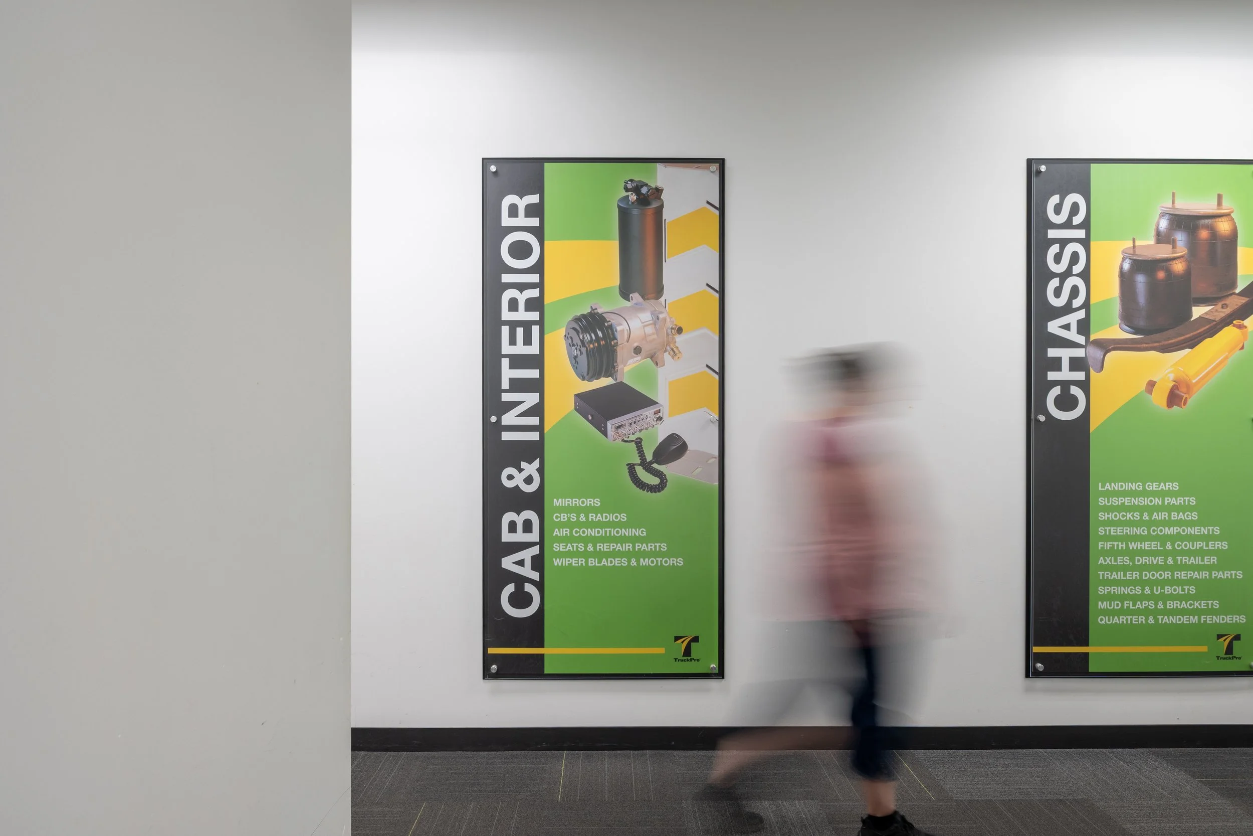 Colorful posters on a wall advertising auto parts, with a person walking past in a blurred motion.