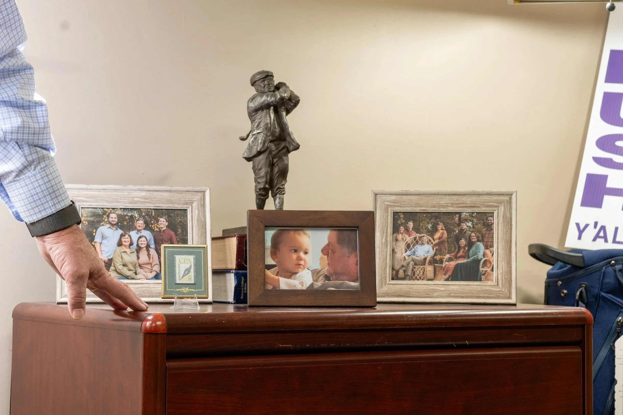 A small wooden table with family photos, a framed picture, and a small statue of a boy playing a flute on top.