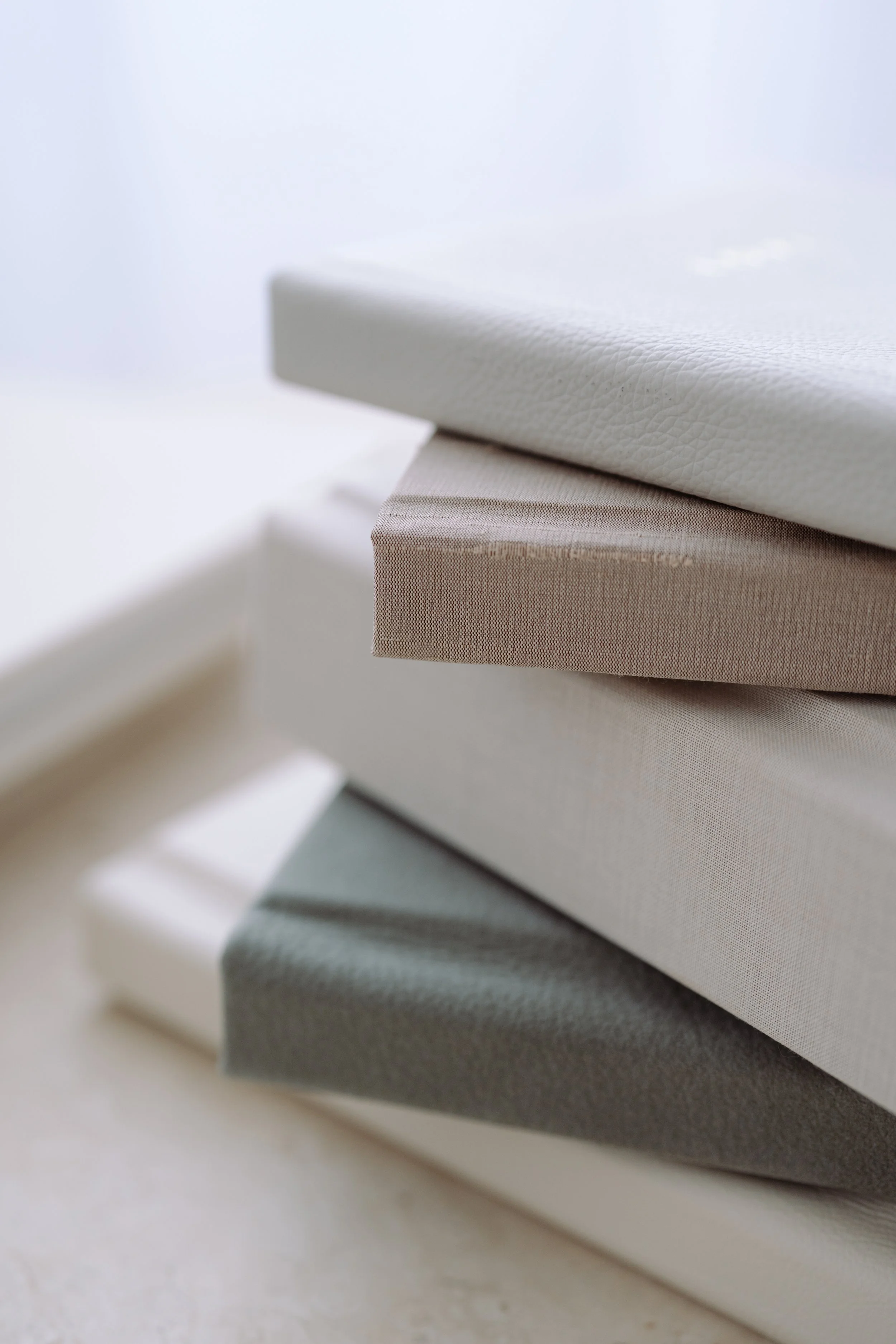 A stack of fabric-covered books or boxes in neutral tones of white, beige, gray, and light brown.